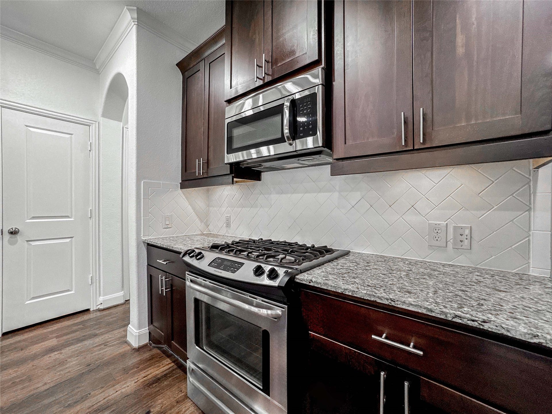 This kitchen features dark wood cabinetry, a sleek granite countertop, stainless steel appliances, and a stylish white subway tile backsplash, offering a modern and functional space.