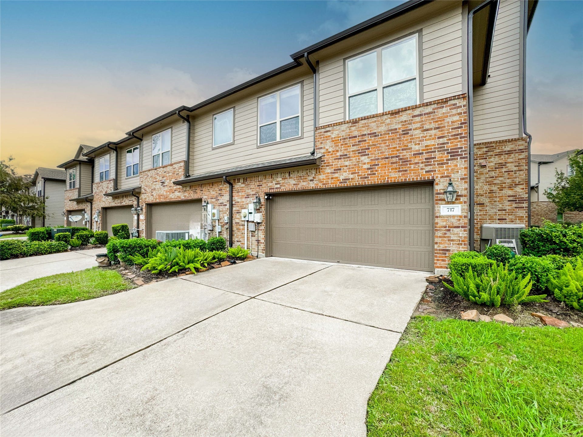 This photo showcases a modern townhouse with a brick facade and attached two-car garage. The property features well-maintained landscaping and a spacious driveway, set in a tidy, suburban neighborhood.