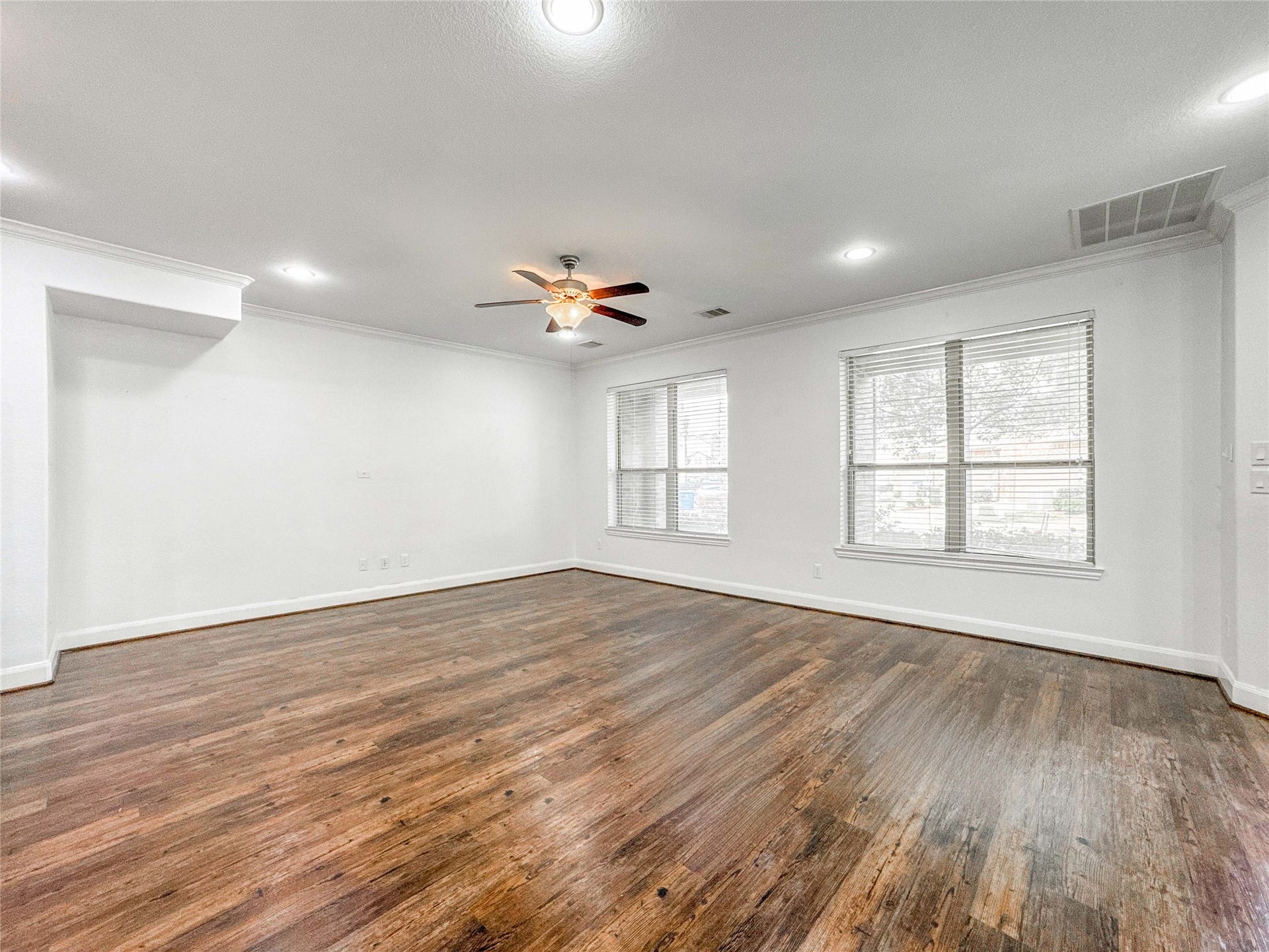 This spacious living room features elegant luxury vinyl floors, fresh white walls, and ample natural light from large windows. A ceiling fan provides comfort, and recessed lighting adds a modern touch.