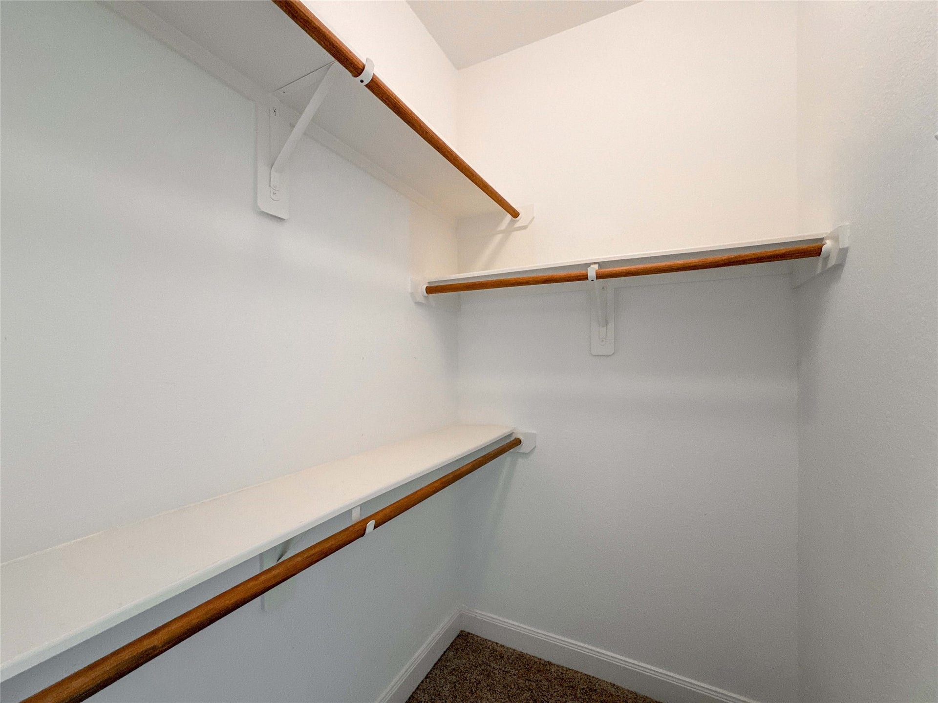 This photo shows a spacious walk-in closet with multiple wooden hanging rods and white shelving, perfect for organized storage.