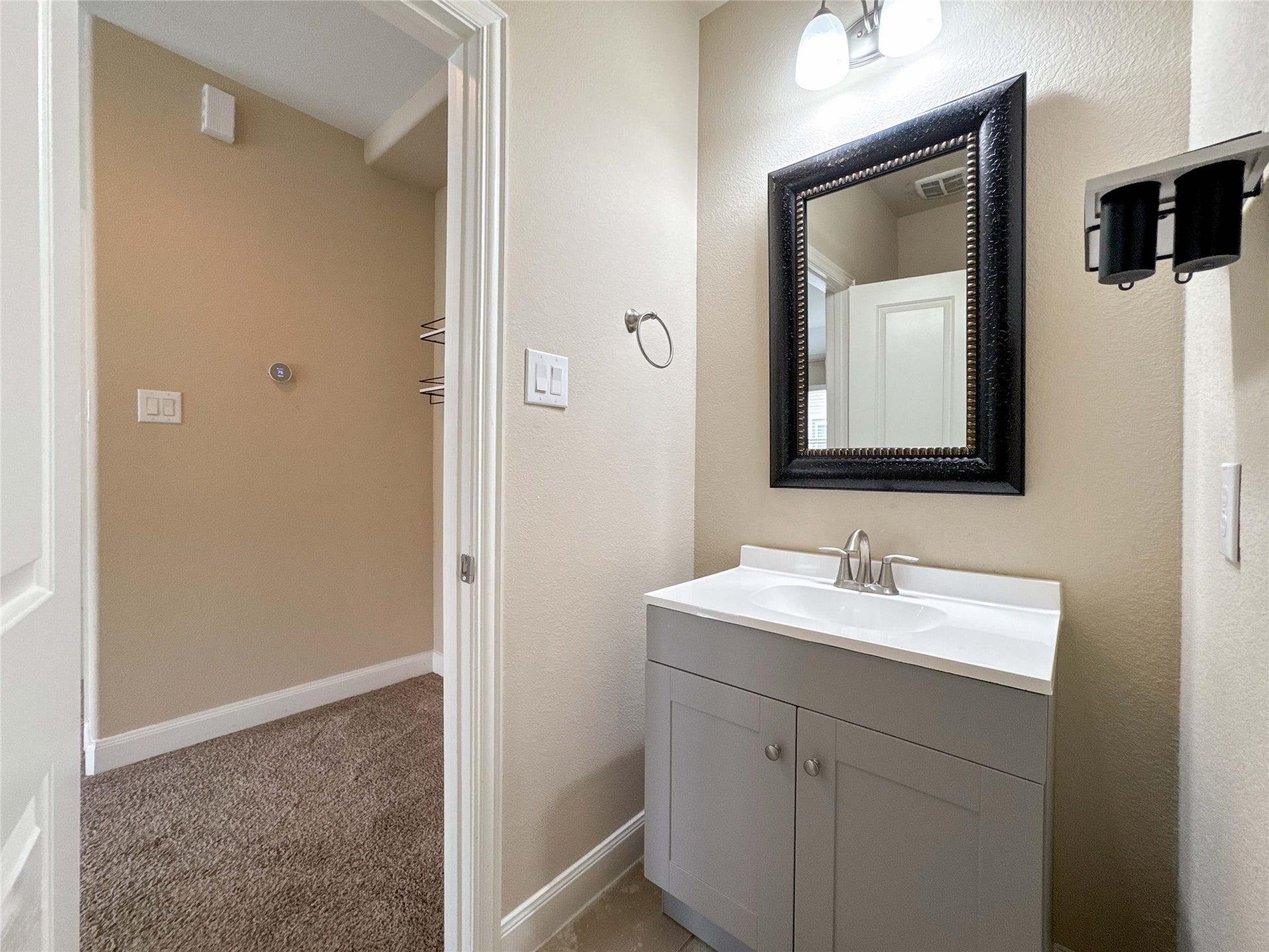 This photo shows a compact bathroom with a modern vanity featuring a white countertop and a sleek faucet. It has a large, decorative framed mirror and neutral wall colors, providing a clean and inviting atmosphere.