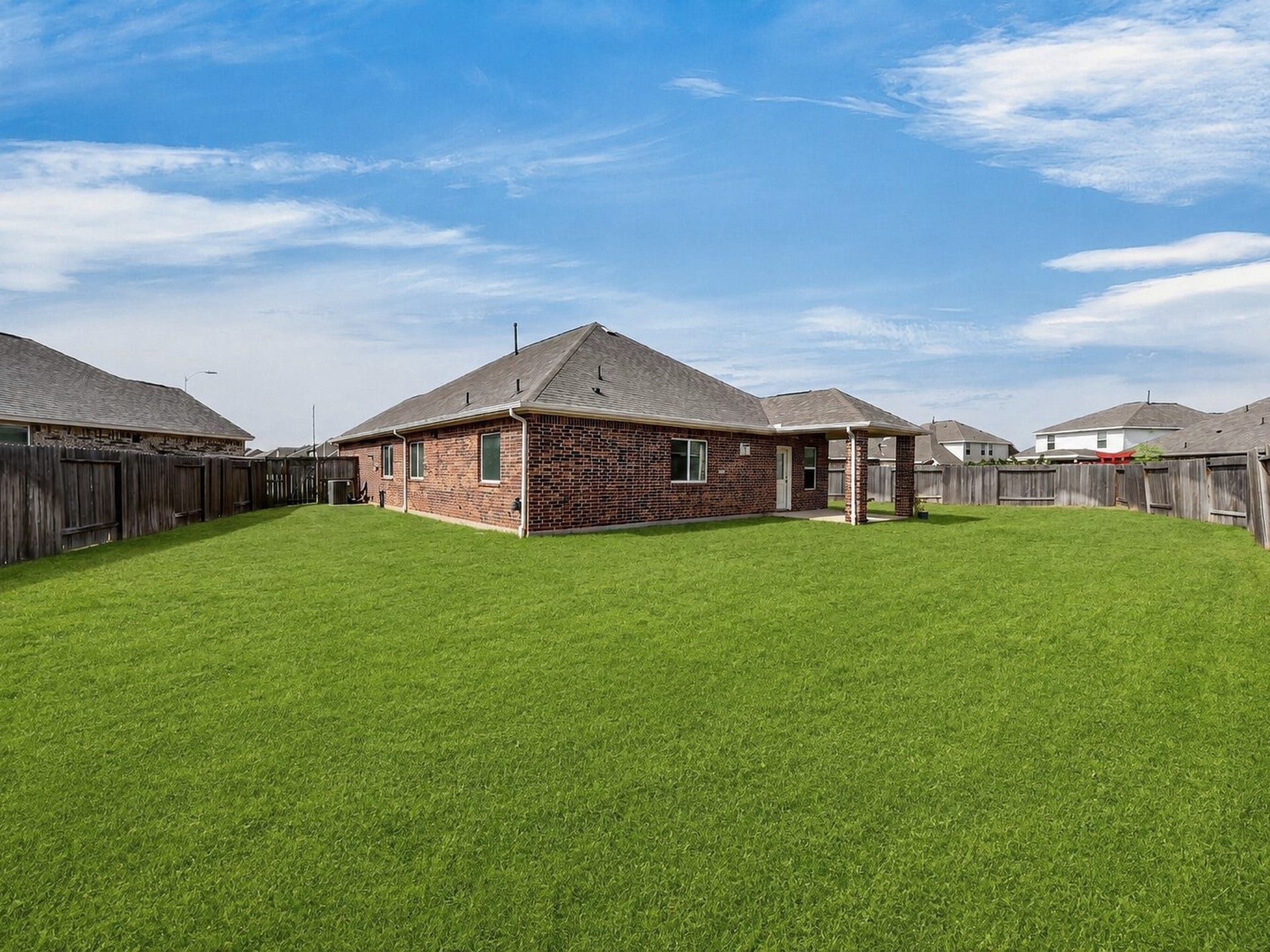 1902 Willow Ridge Lane, Fulshear, TX 77423 Rear exterior view showcases the expansive lawn, covered patio, and fenced backyard.