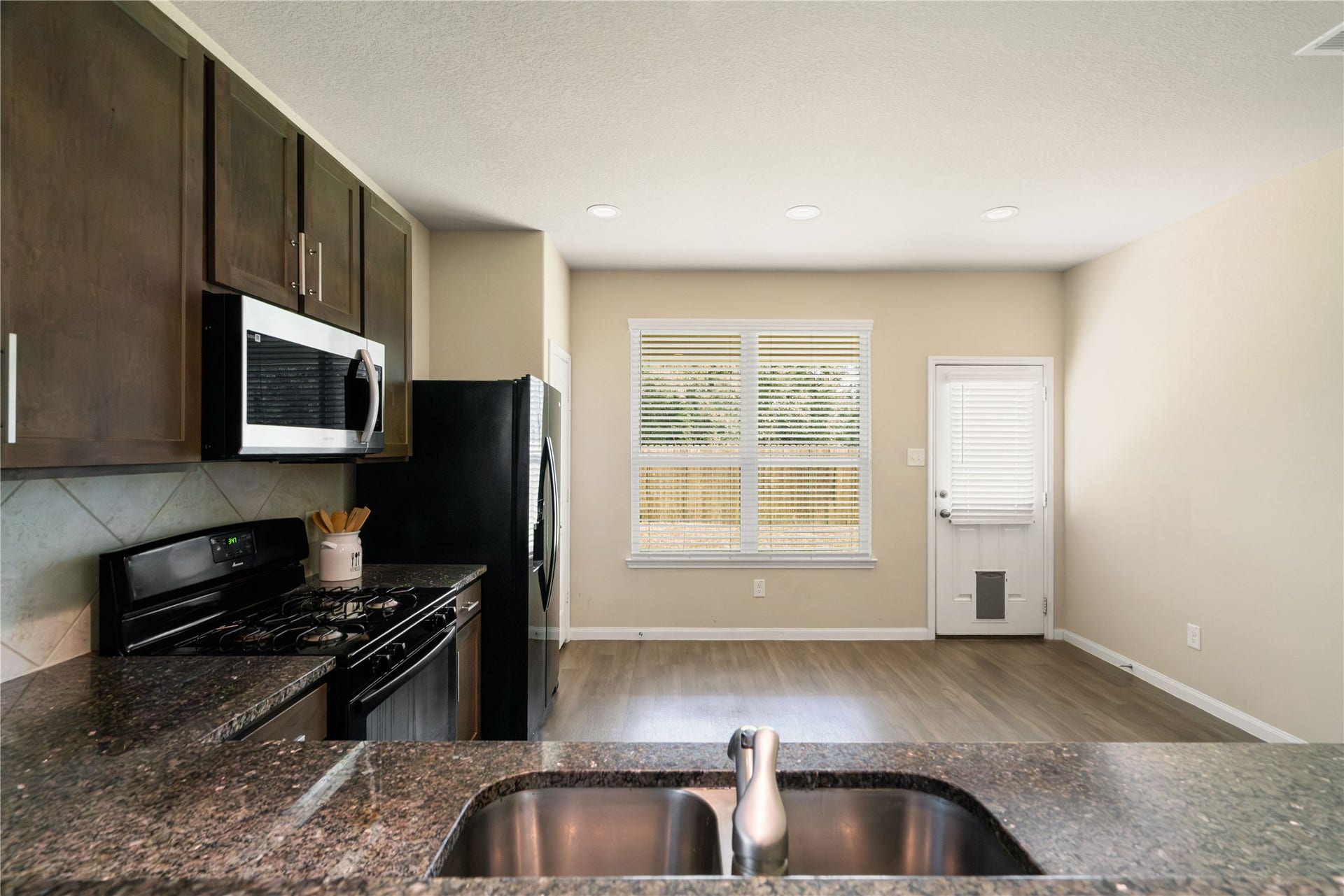 Open kitchen and dining area offers an easy, functional layout with granite countertops, abundant cabinetry, recessed lighting, and plenty of room for a full-size dining table. Large windows bring in natural light, while the open design keeps the kitchen connected to both dining and living spaces.