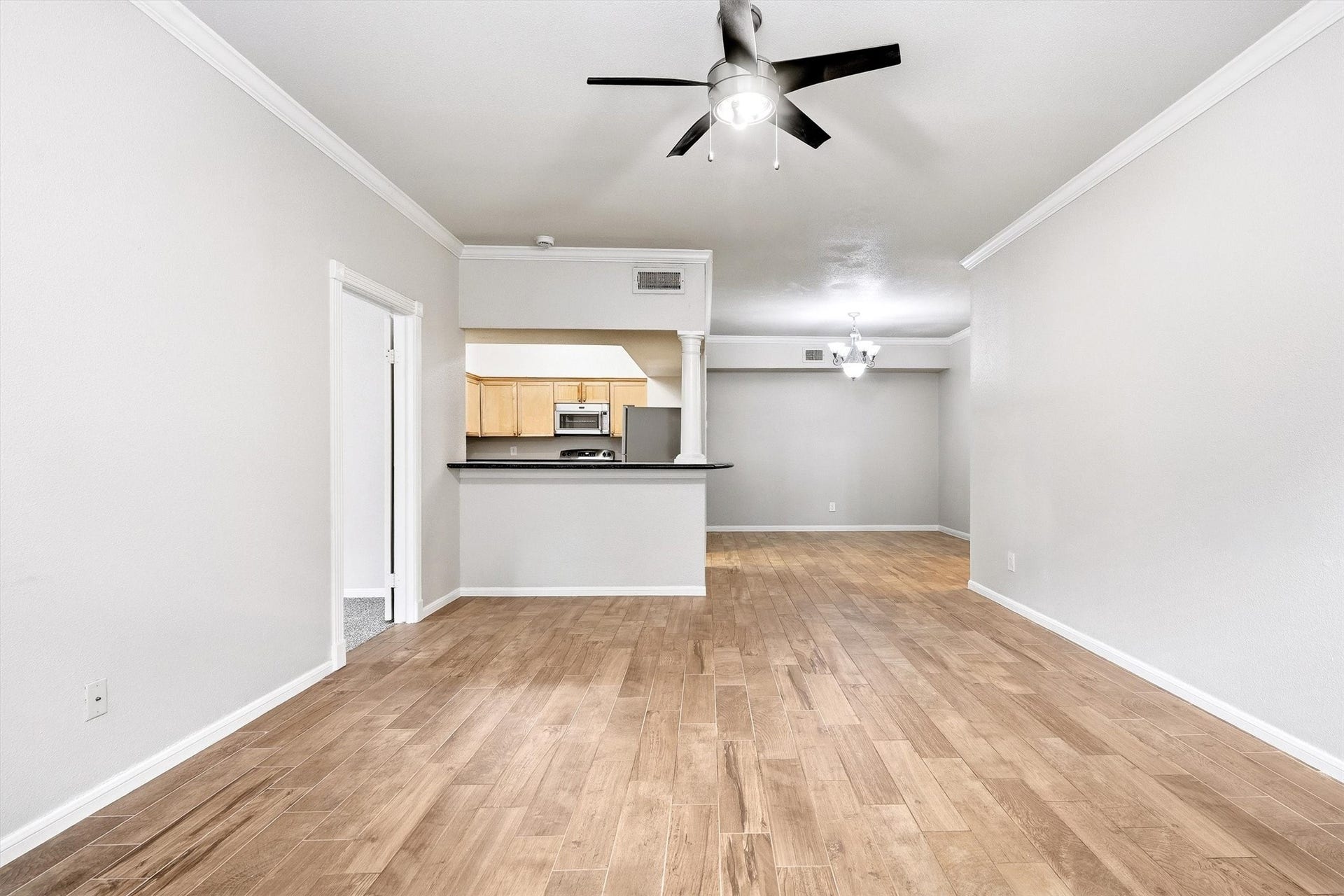 Open living space featuring neutral finishes, crown molding, wood-look flooring, and a convenient breakfast bar.