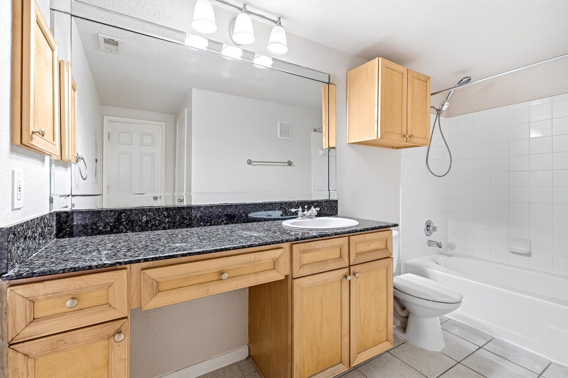 Full bathroom with granite vanity countertop, large mirror, wood cabinetry, tile flooring, and tub/shower combination.