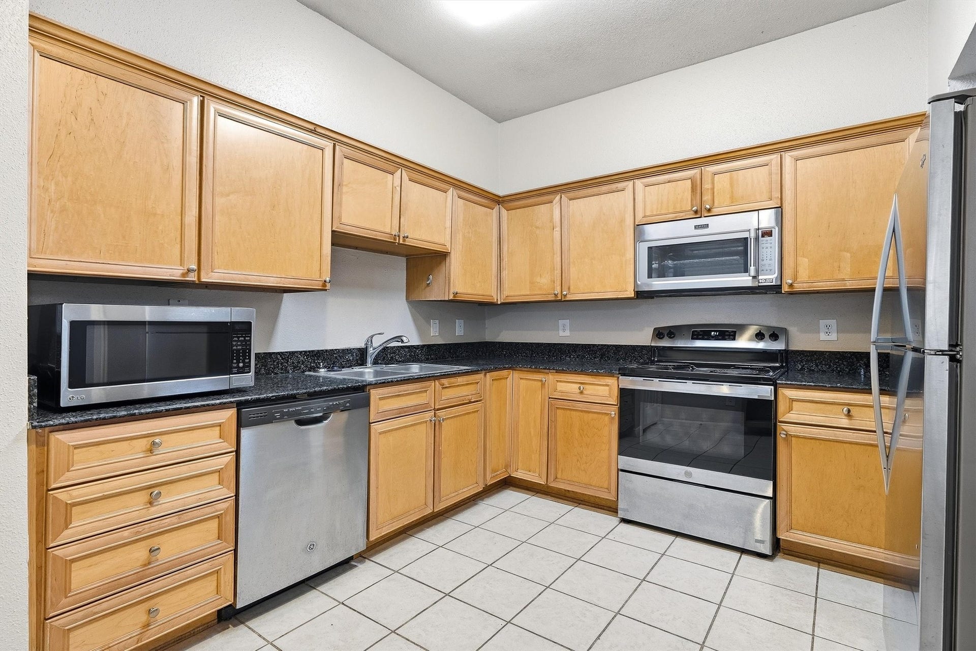 Kitchen features granite countertops, wood cabinetry, stainless steel appliances, double-basin sink, and tile flooring.
