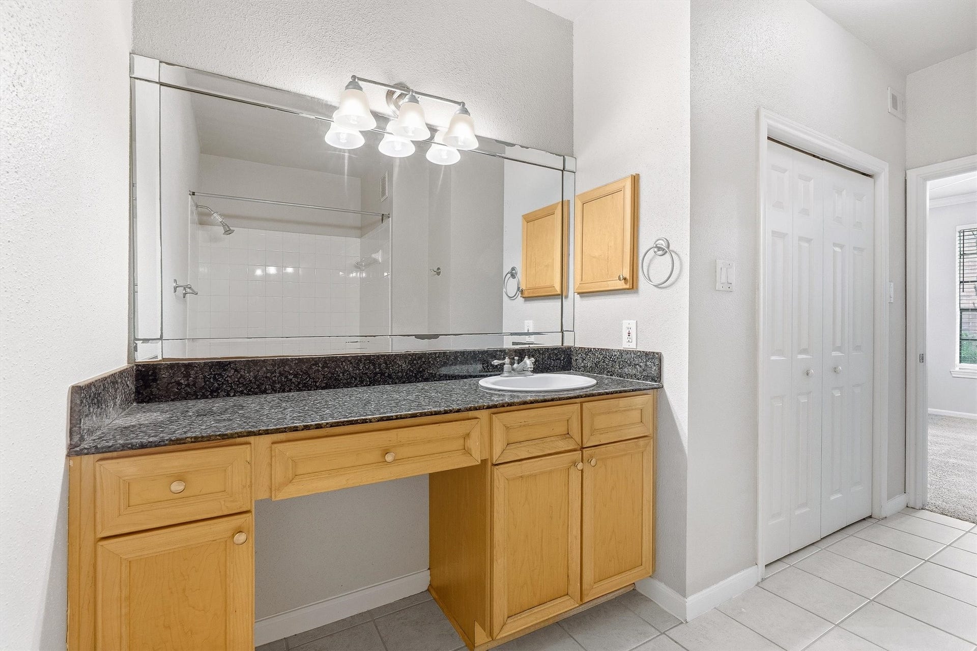 Spacious vanity area with granite countertop, large mirror, wood cabinetry, and convenient storage nearby.