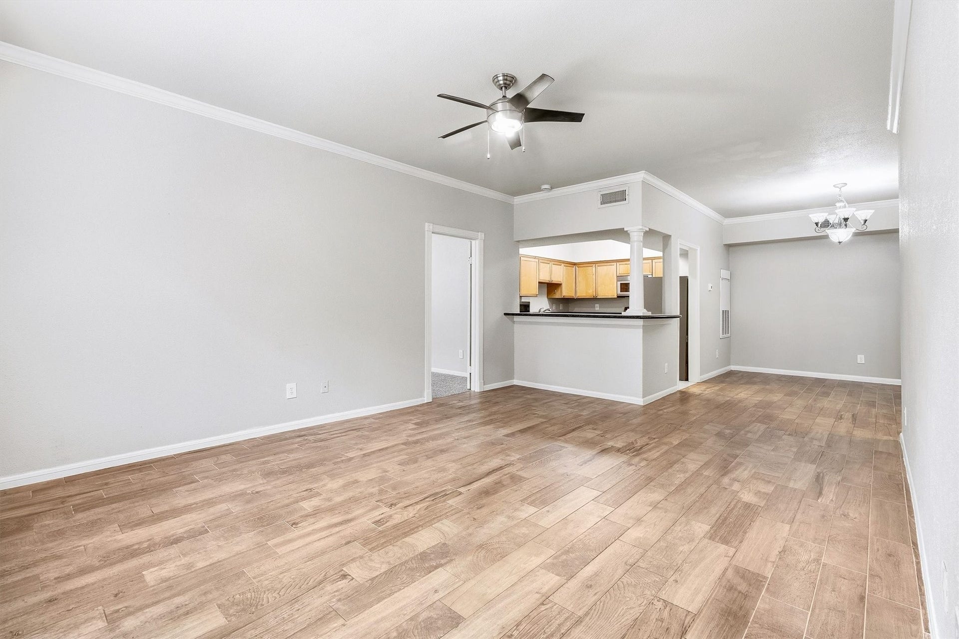 Spacious living area with wood-look flooring, crown molding, ceiling fan, and an open connection to the kitchen and dining area.