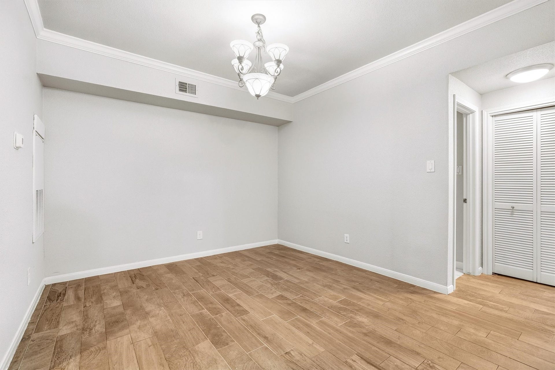 Dedicated dining area with wood-look flooring, crown molding, and decorative chandelier.