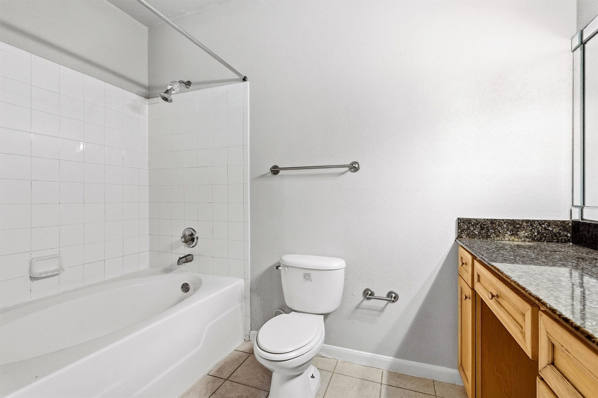 Full bathroom with tub/shower combination, granite-topped vanity, tile flooring, and neutral finishes.