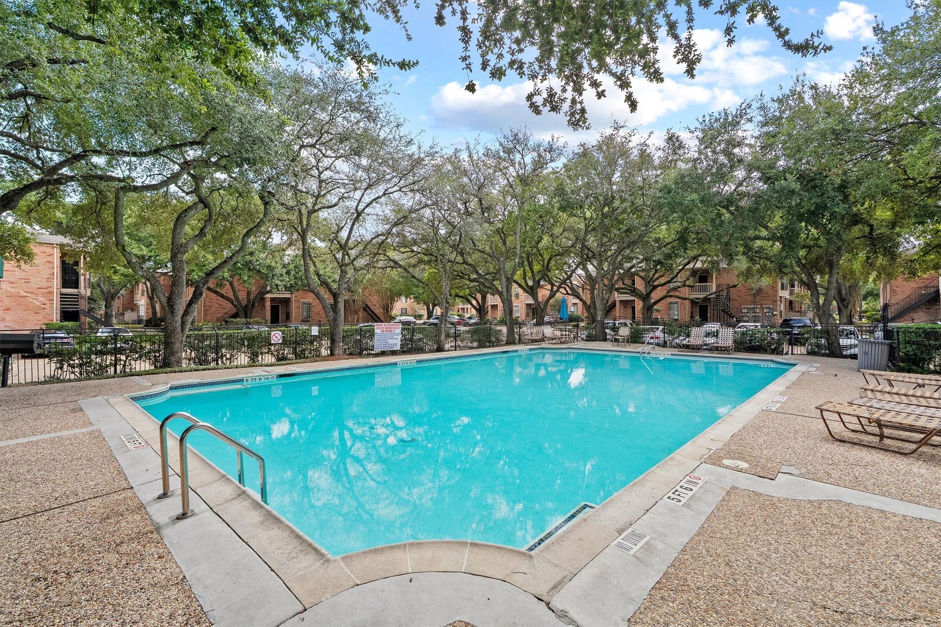 Inviting community pool surrounded by mature shade trees, lounge seating, and landscaped common areas.