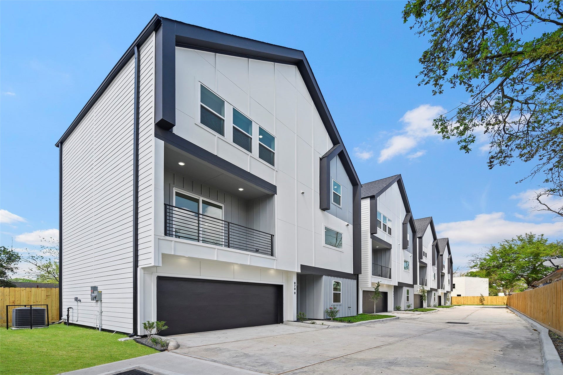 870 W Little York Road, #A, Houston, TX 77091 Modern townhouse with a sleek, angular design, featuring multiple stories and a two-car garage. The exterior is a mix of white and dark accents, with large windows and a small balcony. situated in a row of similar homes. It offers a clean, contemporary look in a well-maintained neighborhood.