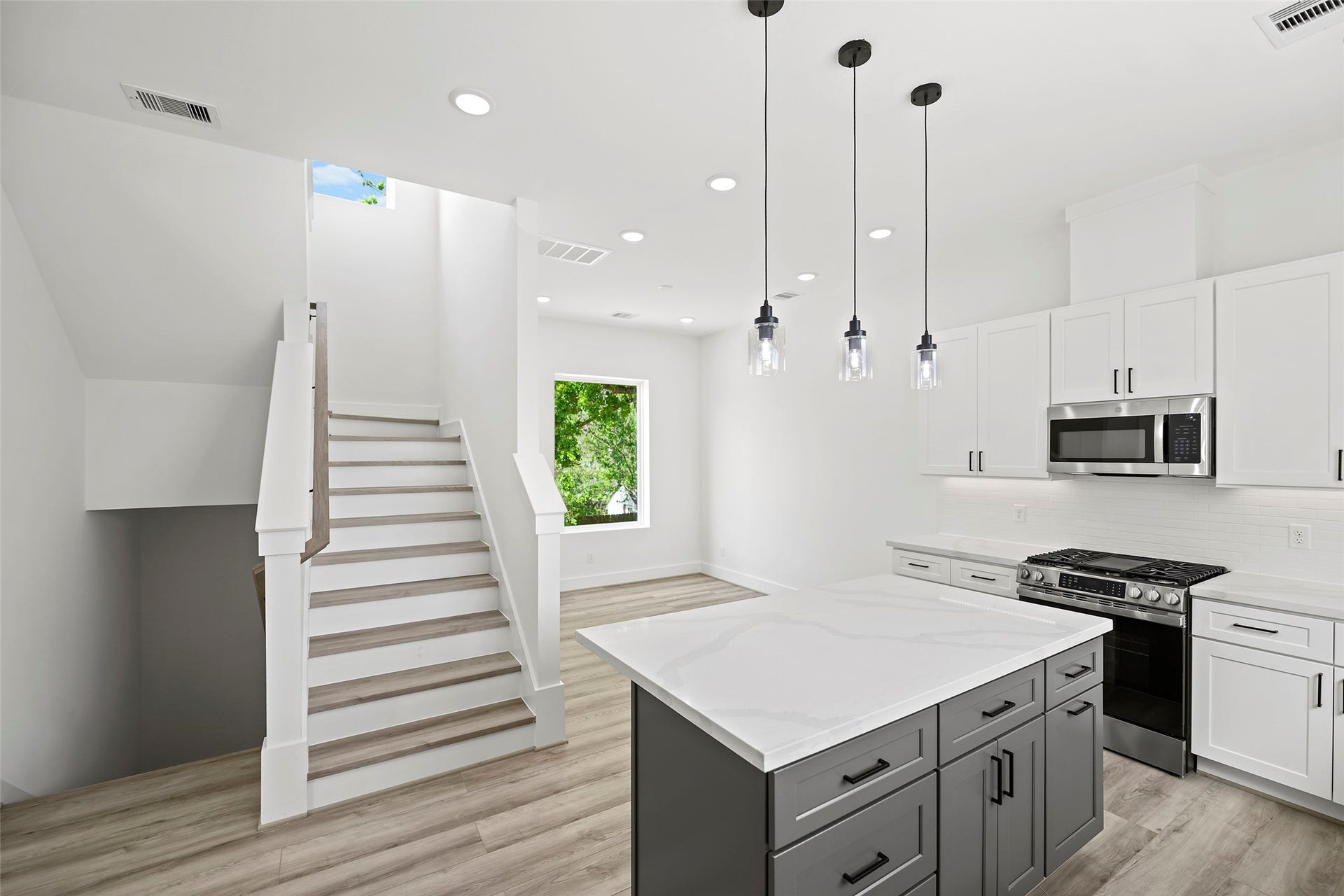 870 W Little York Road, #A, Houston, TX 77091 Bright and modern kitchen with sleek white cabinetry, stainless steel appliances, and a spacious island. The room features elegant pendant lighting and an open staircase, offering a fresh, contemporary feel.