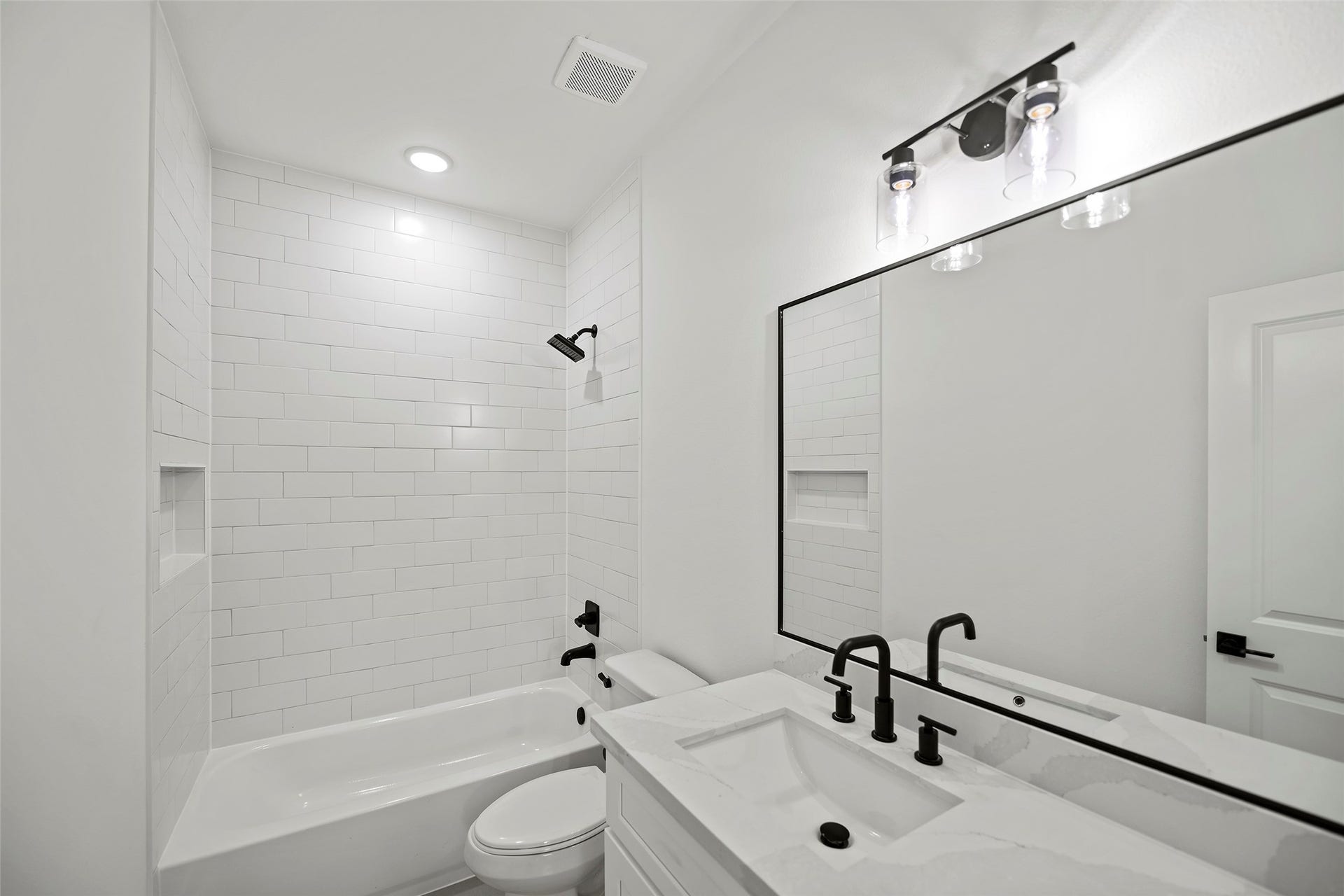 870 W Little York Road, #A, Houston, TX 77091 This first level bathroom features a sleek, modern design with white subway tile walls, a built-in bathtub, and a stylish vanity with a large mirror. Black fixtures add a contemporary touch.