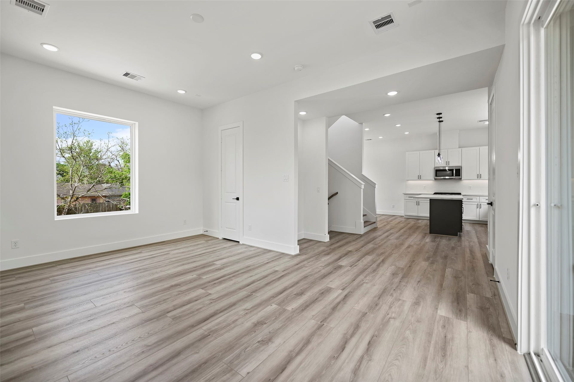870 W Little York Road, #A, Houston, TX 77091 This view from the living area to the kitchen showcases a bright, open-concept living space with modern LVP flooring. The room flows seamlessly into a sleek kitchen featuring white cabinetry, a central island, and stainless steel appliances. Large windows provide natural light, and there's a view of the outdoors.