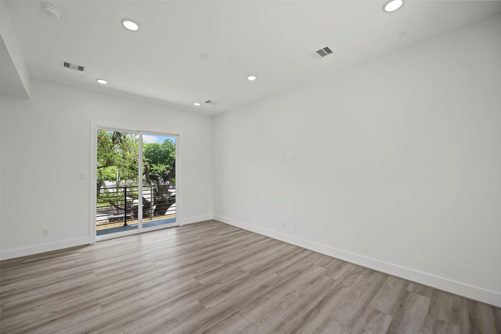 870 W Little York Road, #A, Houston, TX 77091 The living area features modern LVP flooring, recessed lighting, and a large sliding glass door leading to a balcony with a view of lush greenery, creating a bright and inviting space.