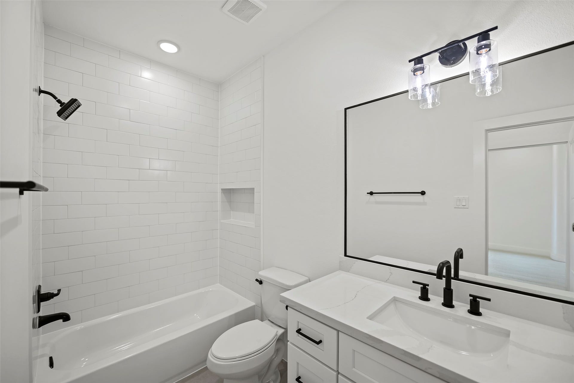 870 W Little York Road, #A, Houston, TX 77091 This modern bathroom features a sleek design with a white subway-tiled shower and a built-in niche. It includes a bathtub, a stylish vanity with a large mirror, and black fixtures for a contemporary look. The room is well-lit with recessed lighting and decorative light fixtures.