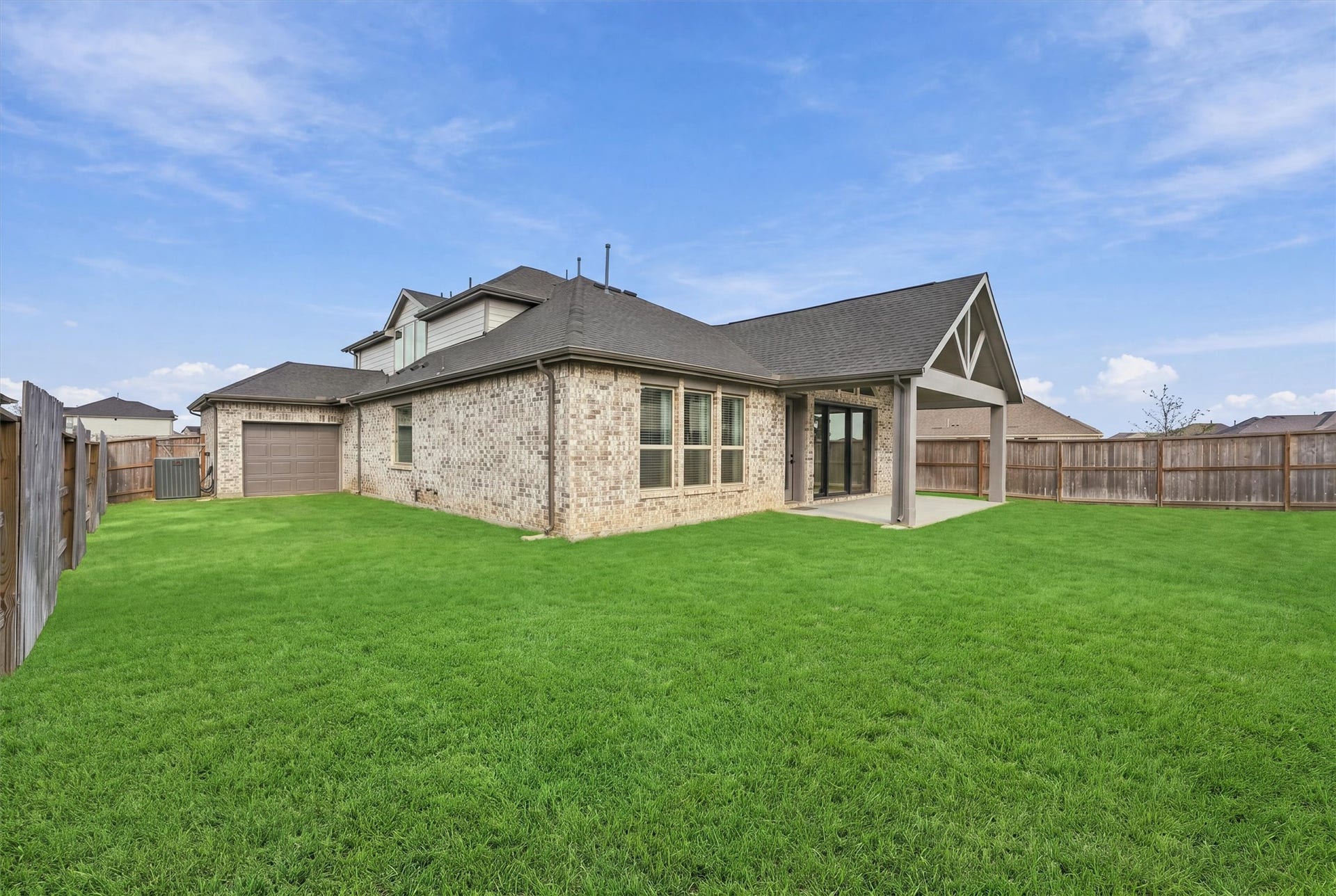 The brick rear elevation has a covered patio and a large fenced backyard, plus a garage door at the drive-through bay.