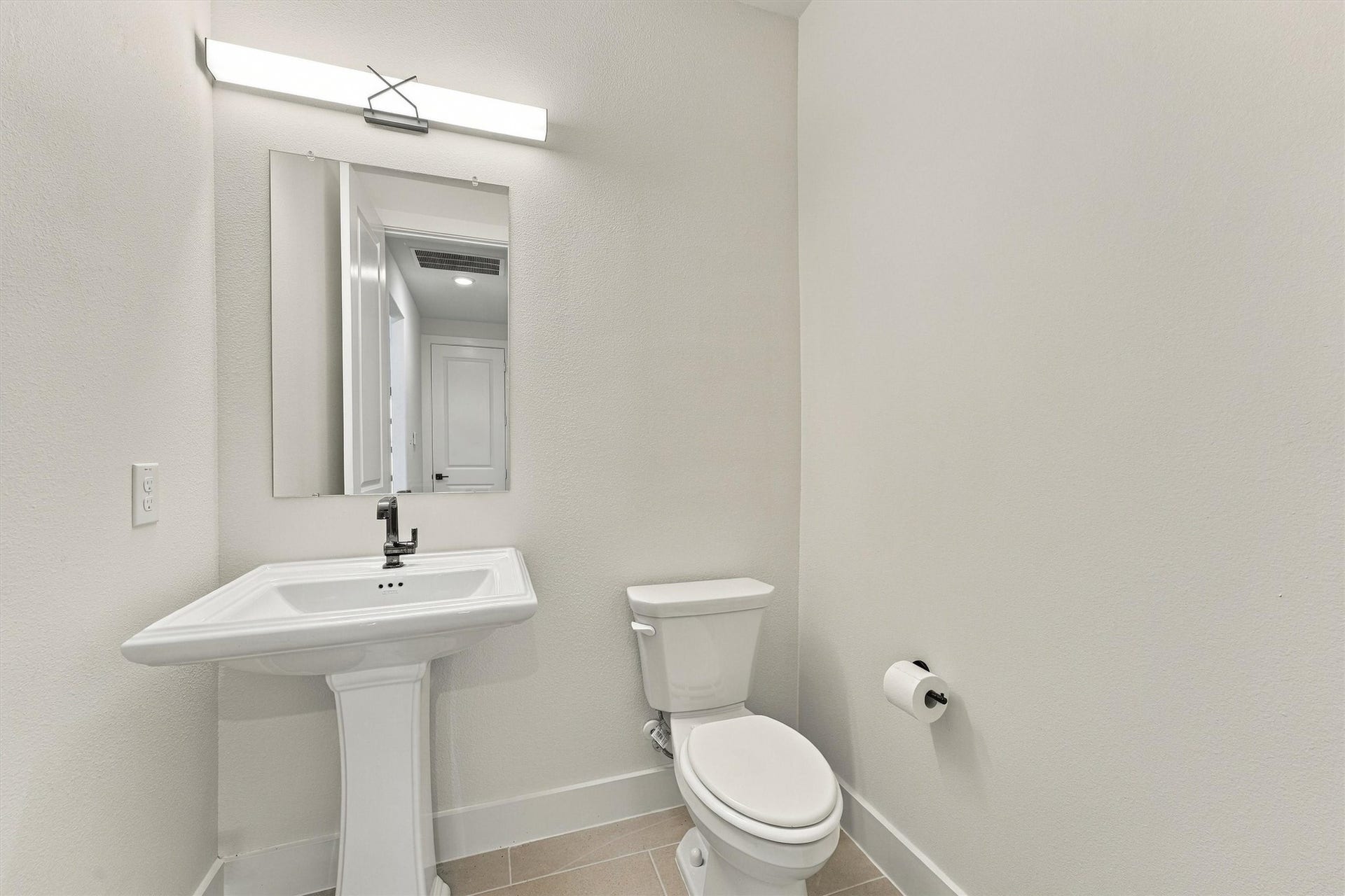 A classic pedestal sink and modern sconce lighting create a refined powder room for guests.