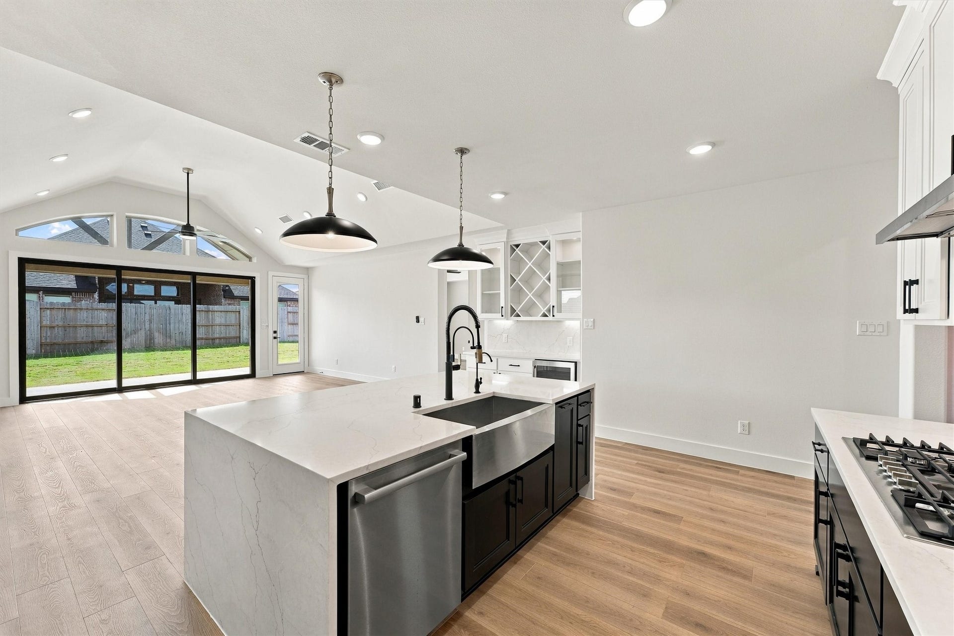 A farmhouse sink with a pro-style faucet anchors the island, which looks out to the vaulted living area and the wall of glass doors.