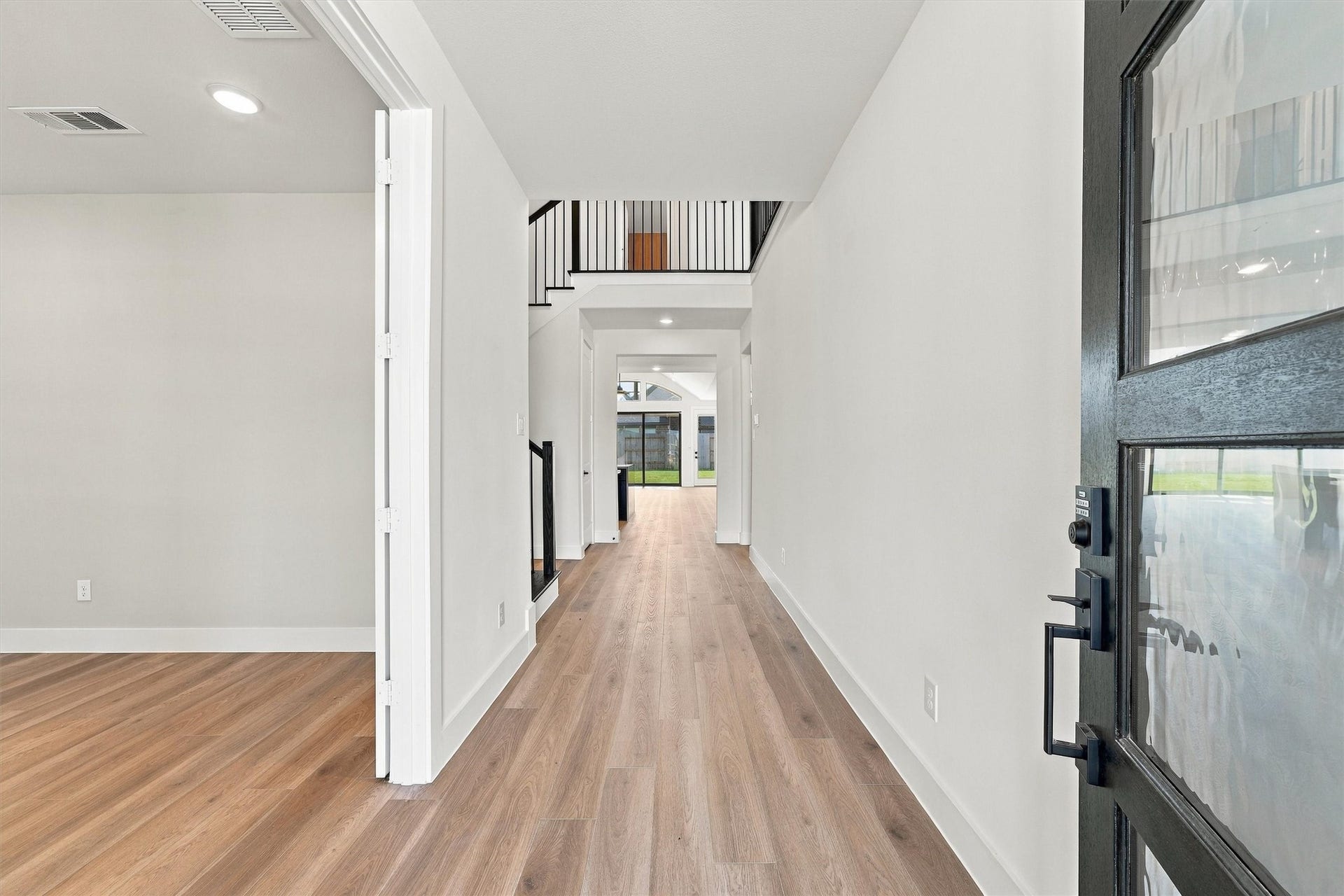 A gallery entry with an open stairwell and modern black balusters, and sightlines straight through to the backyard.
