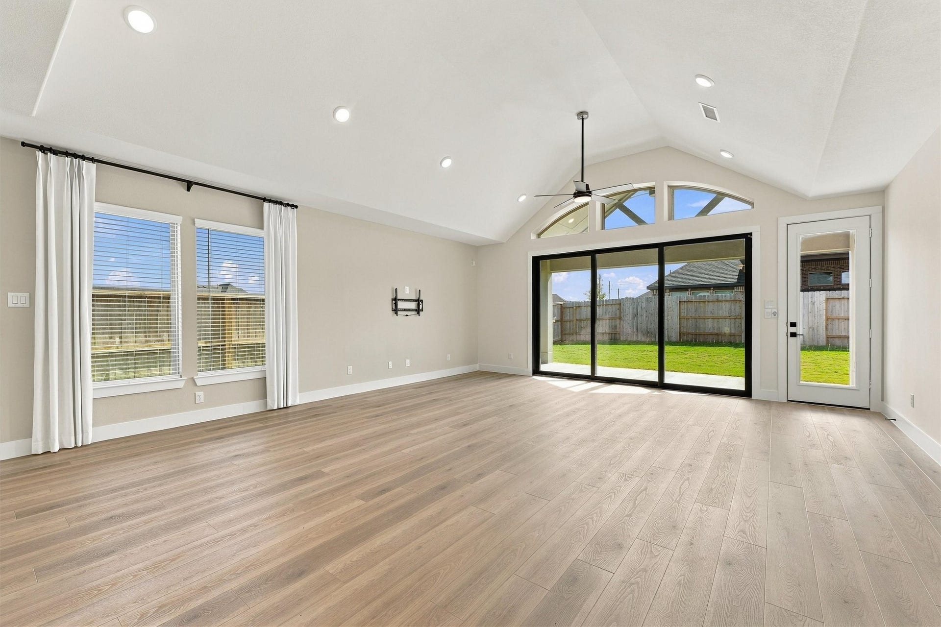 Vaulted ceilings and arched transom windows rise above multi-slide glass doors that open to the covered patio for seamless indoor-outdoor entertaining.