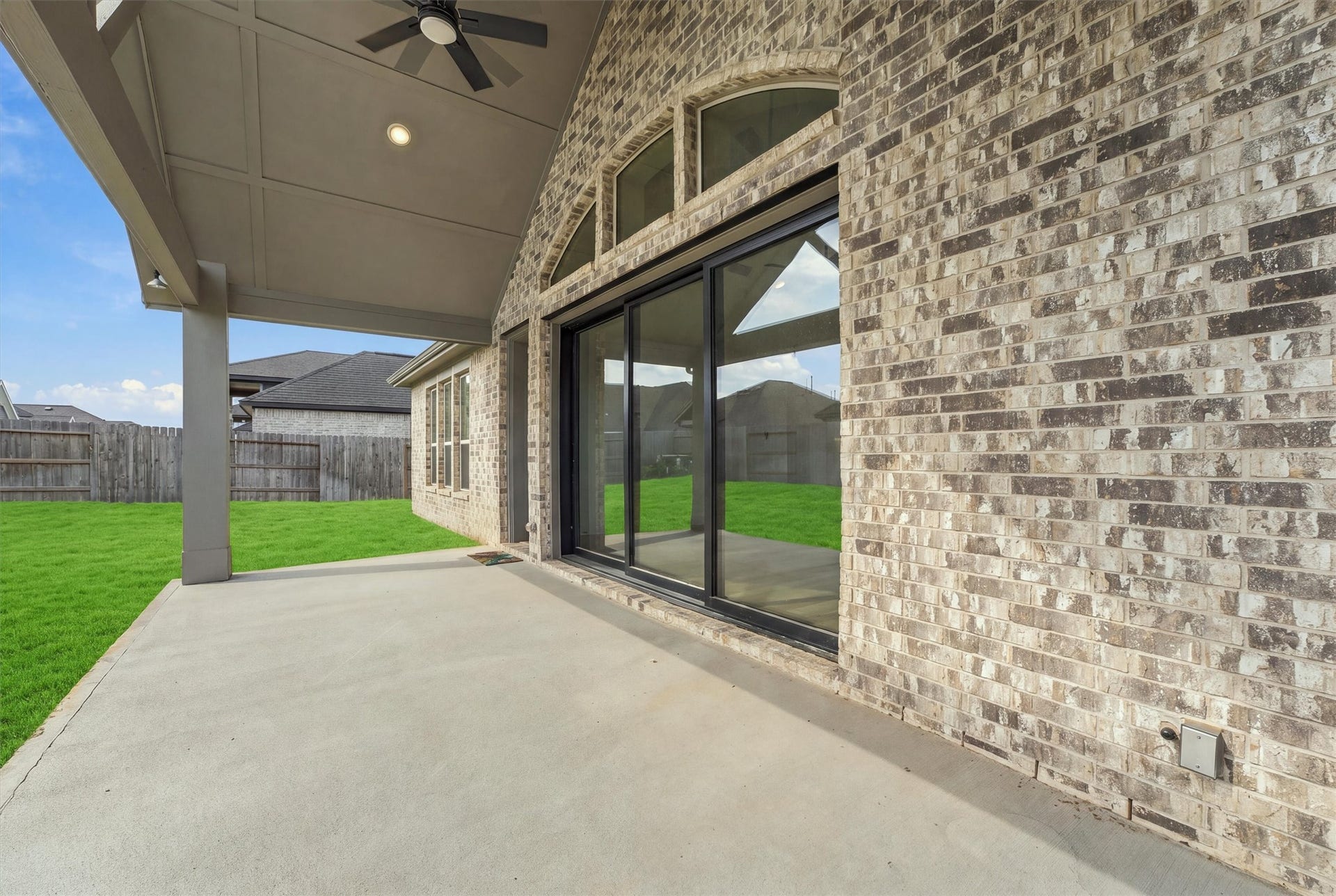 A gabled patio with a ceiling fan and recessed lighting sits under arched transom windows, and multi-slide glass doors open it to the living room.