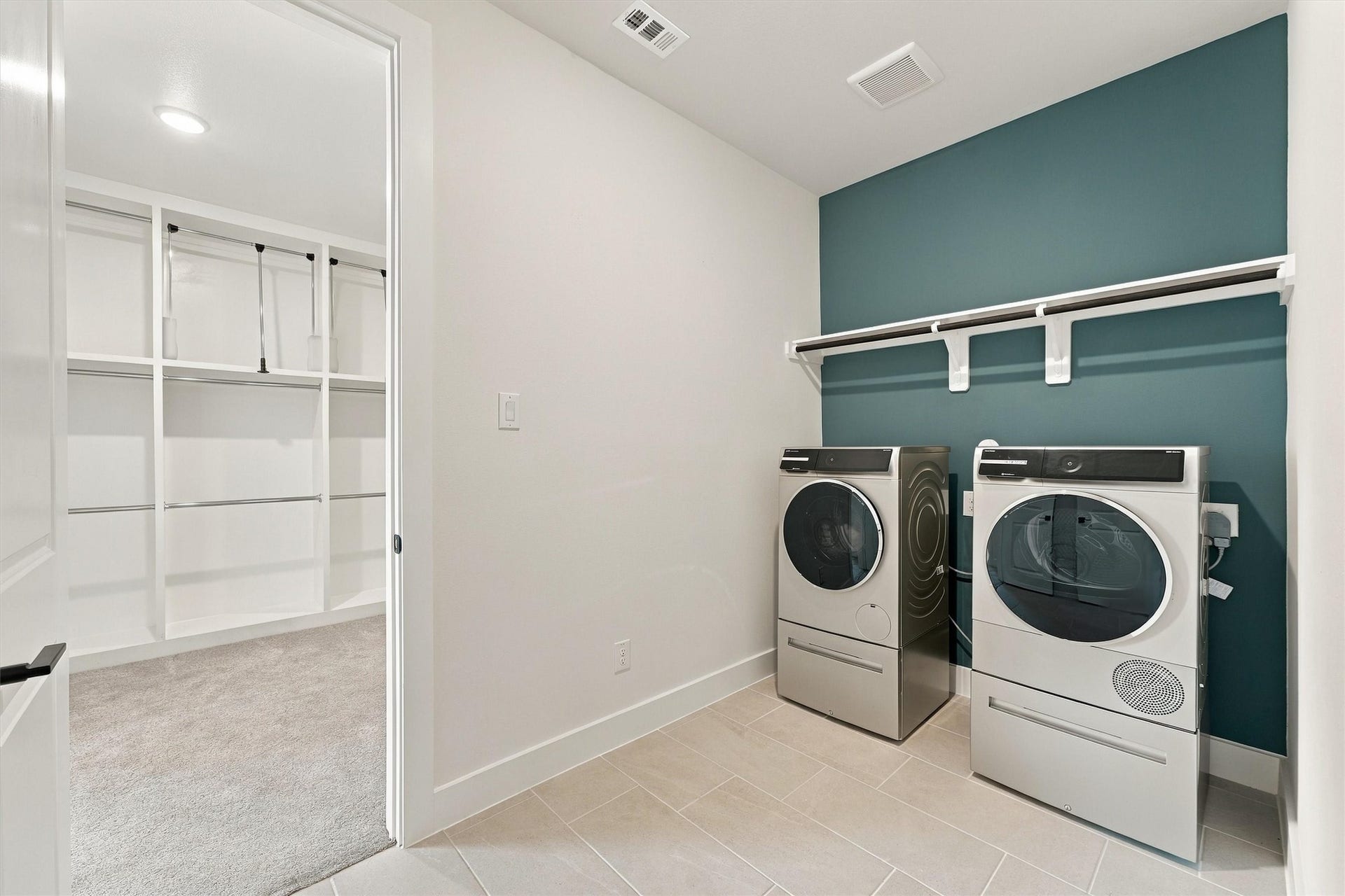 A teal accent wall, tile floors, and a hanging rod, with direct access to the primary closet.