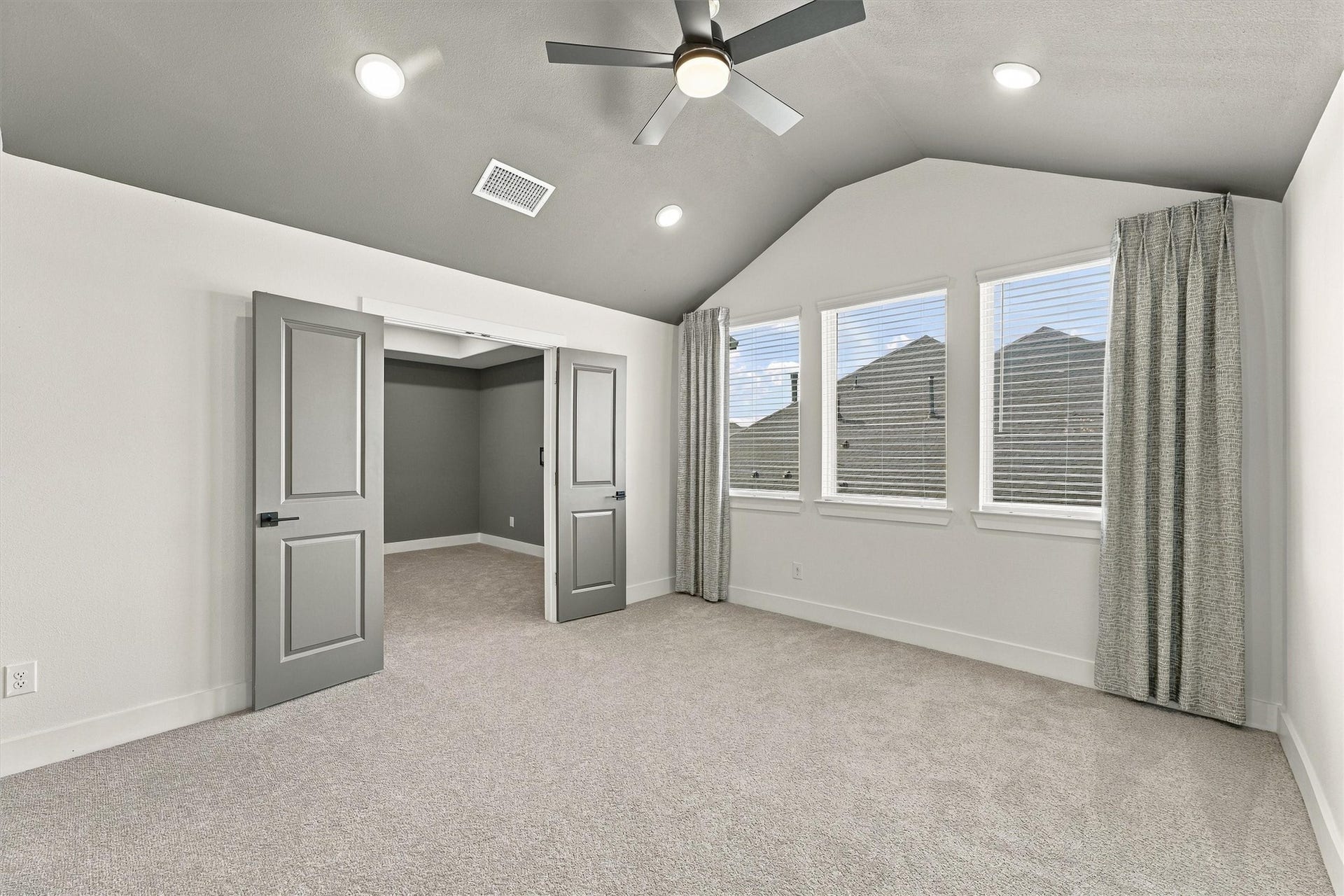 A vaulted game room with a ceiling fan, recessed lighting, and a wall of windows. Double doors open to the media room.