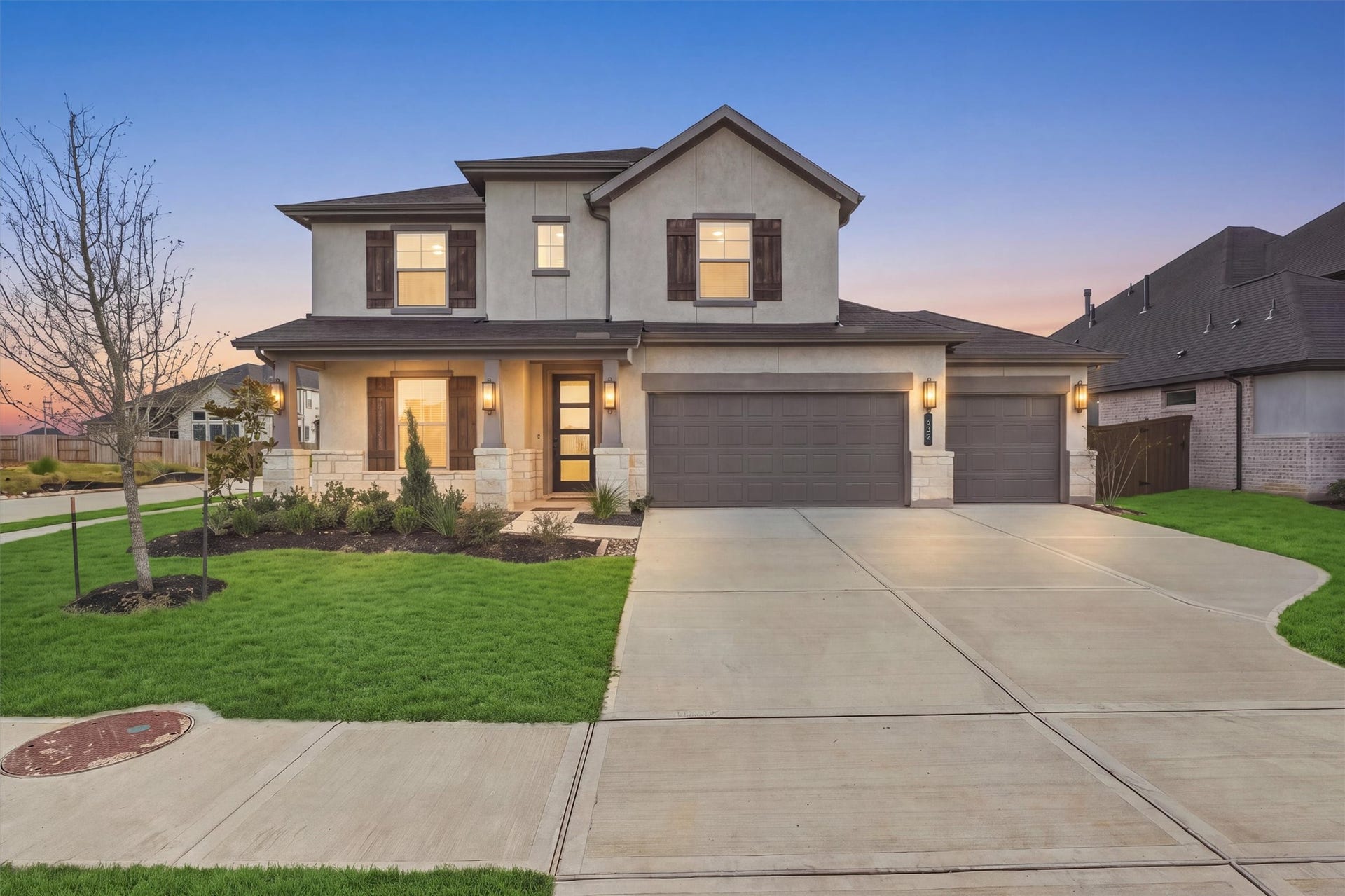 Welcome Home: Stone accents, stucco, and cedar-tone shutters create striking curb appeal, and the lantern sconces glow across a covered front porch.