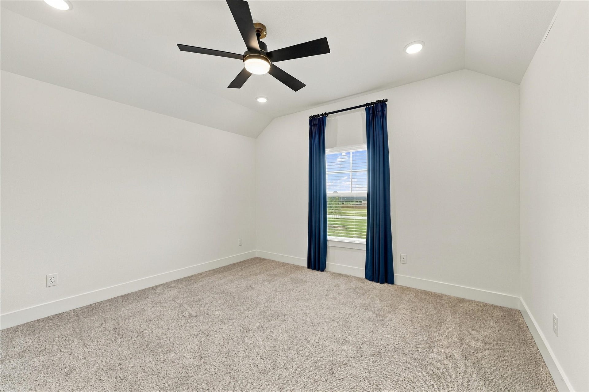 A vaulted bedroom with a ceiling fan, recessed lighting, and tailored navy drapery.