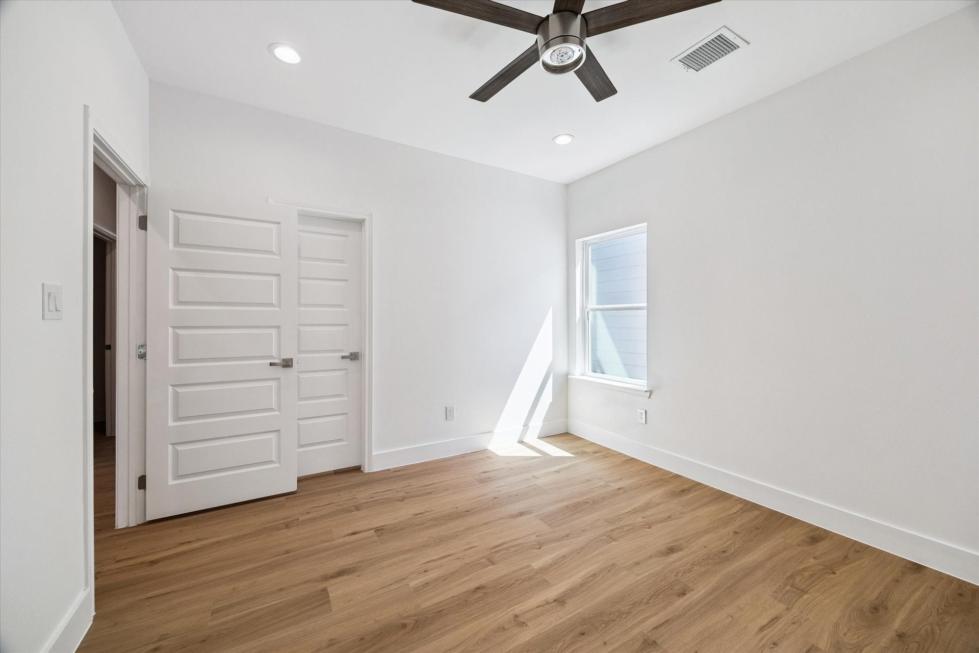 5310 Salina Street, Houston, TX 77026 Another view of the secondary bedroom highlights its efficient layout, warm flooring, and crisp modern finishes. Natural light enters through the window, while a contemporary ceiling fan and recessed lighting provide comfort and convenience. Multiple doors offer access to surrounding spaces and storage, while the neutral palette creates an easy backdrop for any decorating style.