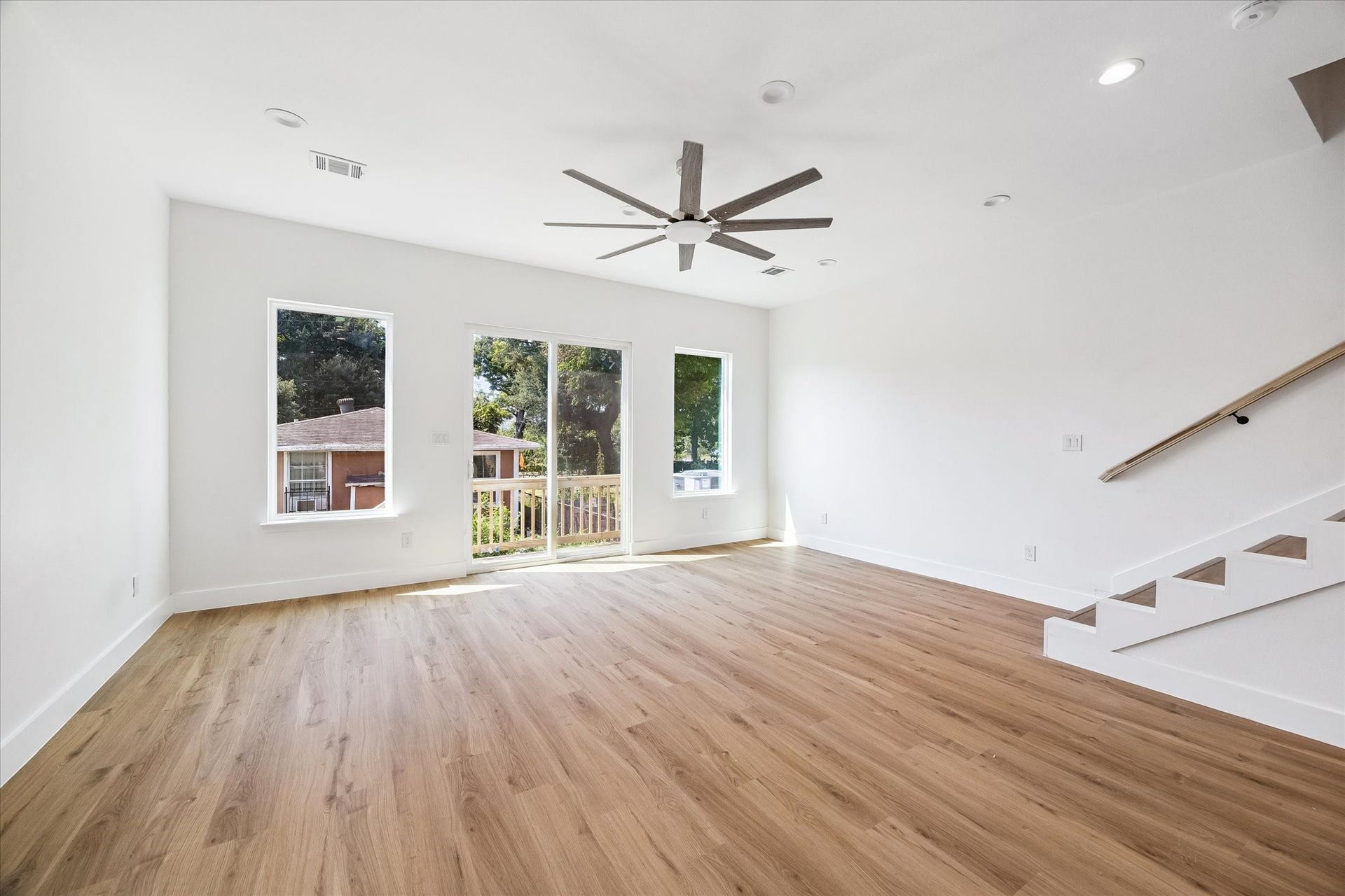 5310 Salina Street, Houston, TX 77026 The open-concept living room offers generous space for relaxing, entertaining, or creating multiple seating zones. Large windows and sliding glass doors fill the room with natural light and provide access to the outdoor balcony. Warm wood-look flooring extends throughout the space, while recessed lighting and a contemporary ceiling fan complete the modern design. The staircase nearby creates an easy connection between levels.