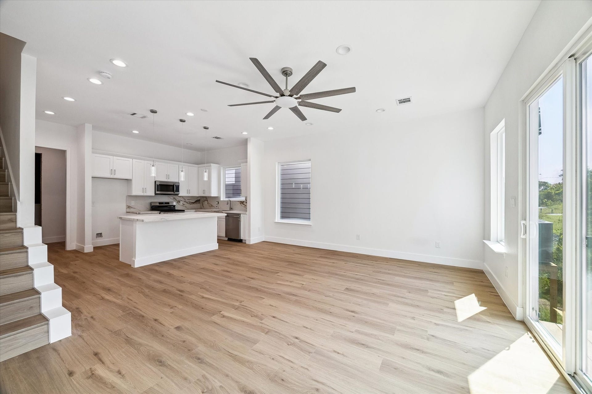5310 Salina Street, Houston, TX 77026 From this angle, the open layout between the living area and kitchen truly shines. A spacious footprint allows plenty of room for comfortable seating and dining arrangements, while the large ceiling fan adds style and everyday comfort. Natural light pours in through expansive windows and glass doors, highlighting the warm flooring and crisp neutral walls. The kitchen remains visually connected for easy conversation and entertaining.