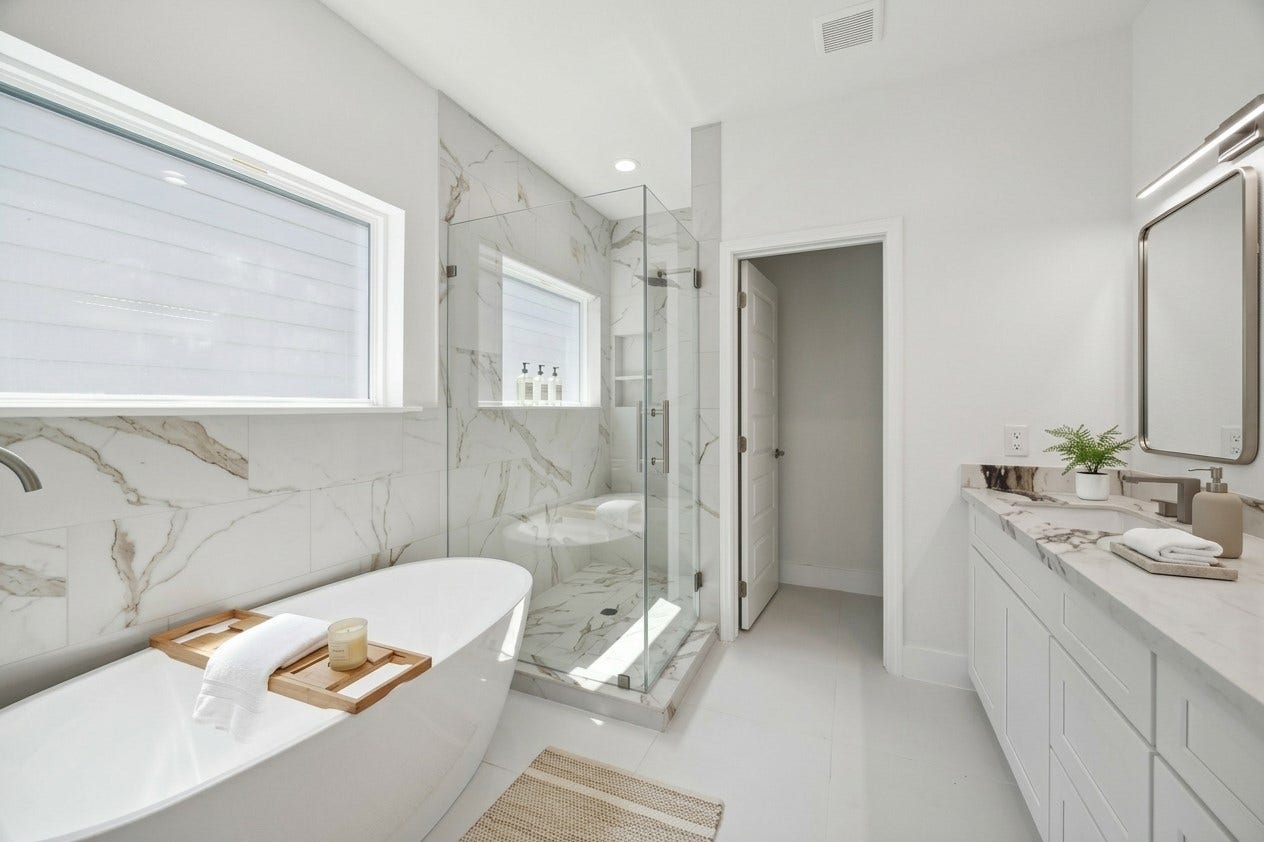 5310 Salina Street, Houston, TX 77026 The primary bathroom delivers a spa-inspired atmosphere with a freestanding soaking tub, frameless glass shower, and striking marble-look tile carried across the walls and shower floor. Natural light streams through multiple windows, while the long vanity provides generous storage and counter space. Sleek fixtures and a bright neutral palette complete this polished, contemporary retreat.