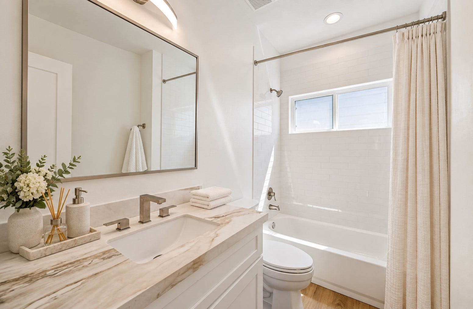 5310 Salina Street, Houston, TX 77026 This bright full bathroom features a clean white vanity with a marble-look countertop, under-mount sink, and sleek modern faucet. The tub and shower combination is surrounded by glossy white subway-style tile extending toward the ceiling for a polished finish. A horizontal window introduces natural light, while recessed and vanity lighting keep the space bright and functional.