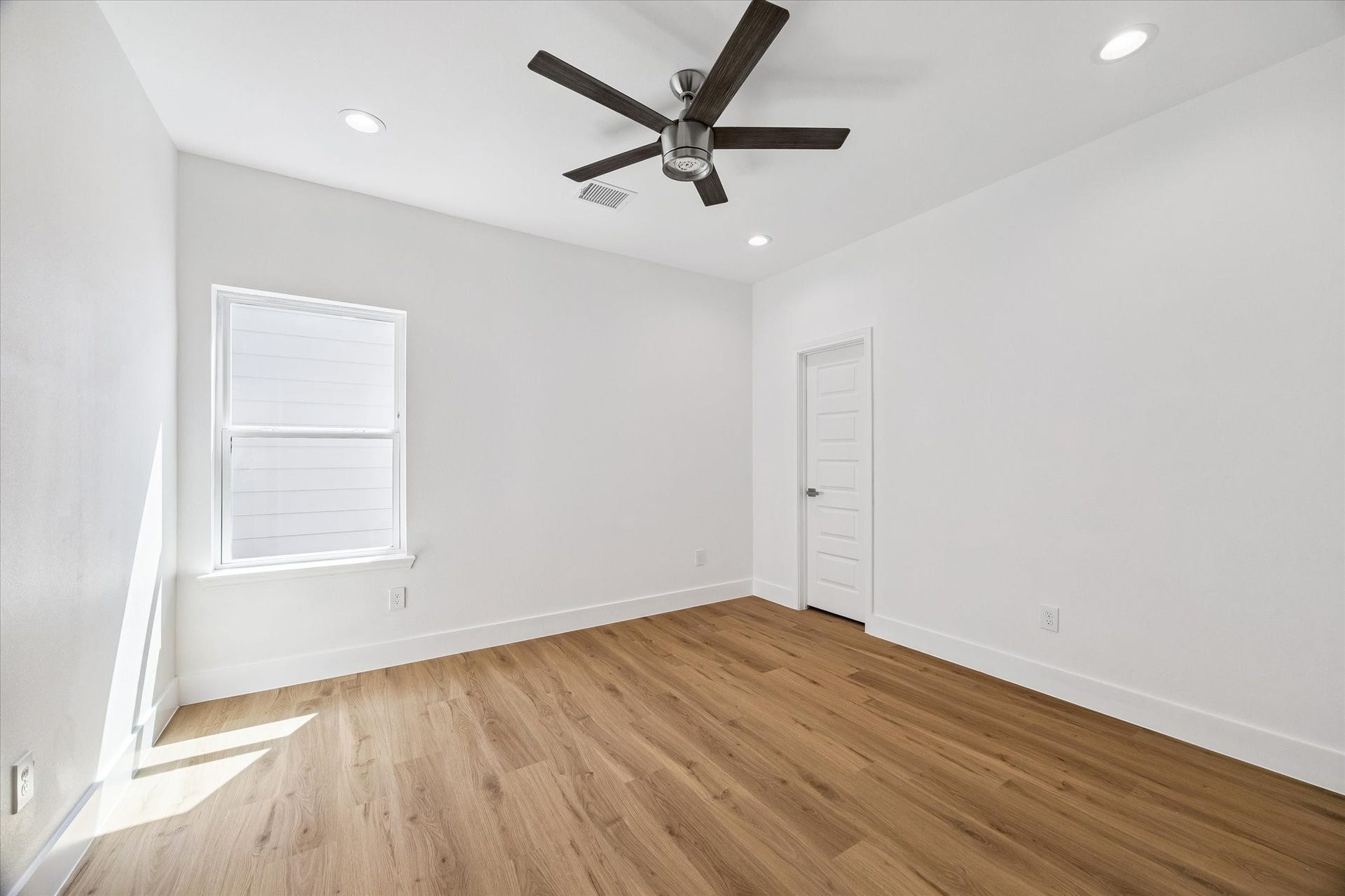5310 Salina Street, Houston, TX 77026 This bright secondary bedroom offers warm wood-look flooring, neutral walls, and a modern ceiling fan for a clean contemporary feel. A large window brings in natural light, while recessed lighting adds additional illumination. The simple, spacious layout provides flexibility for bedroom furnishings, a home office arrangement, or a comfortable guest retreat.