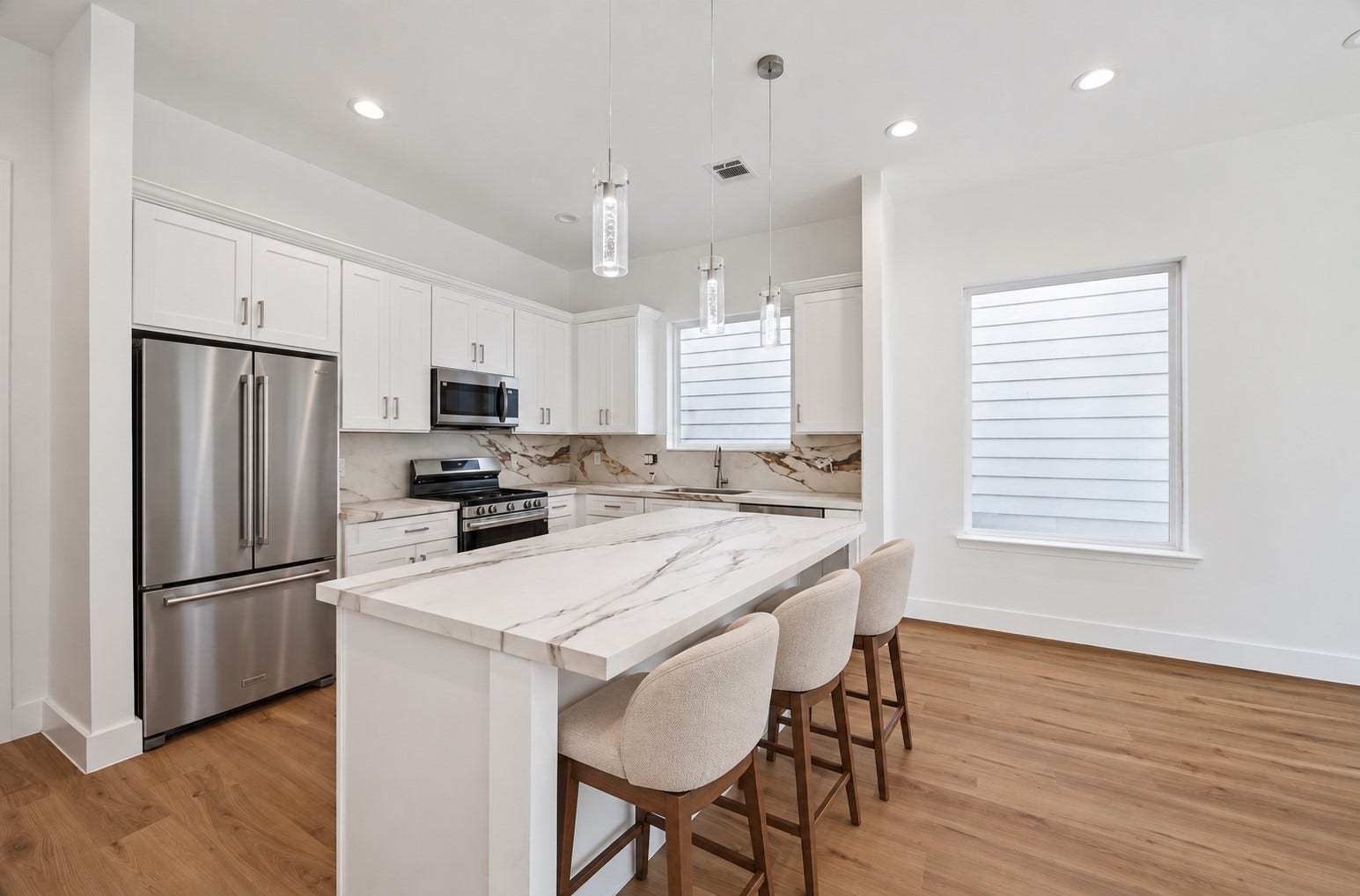 5310 Salina Street, Houston, TX 77026 The kitchens oversized island becomes a natural centerpiece for gathering, dining, and meal preparation. Marble-look countertops pair beautifully with crisp white cabinetry, stainless steel appliances, and sleek modern hardware. Pendant lights add a decorative touch above the island, while recessed lighting and large windows keep the room bright. Warm wood-look flooring brings balance and warmth to the contemporary palette.