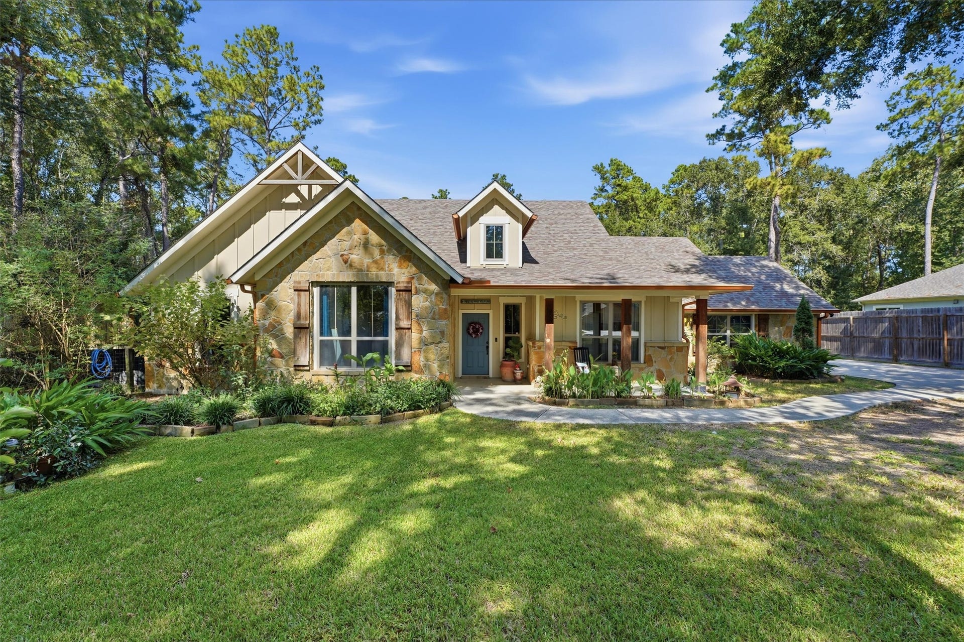 Charming home with a stone-accented facade, nestled among mature trees, featuring a well-maintained lawn and inviting front porch for relaxing outdoors.