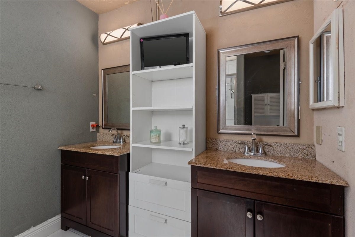9522 Wellsworth Drive, Houston, TX 77083 Primary Bathroom with dual wood vanities, built-in storage shelving, and framed mirrors