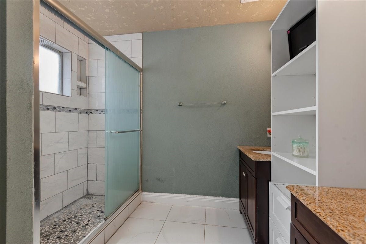 9522 Wellsworth Drive, Houston, TX 77083 Primary bath with walk-in shower, frosted glass enclosure, pebble-tile floor, and built-in shelving