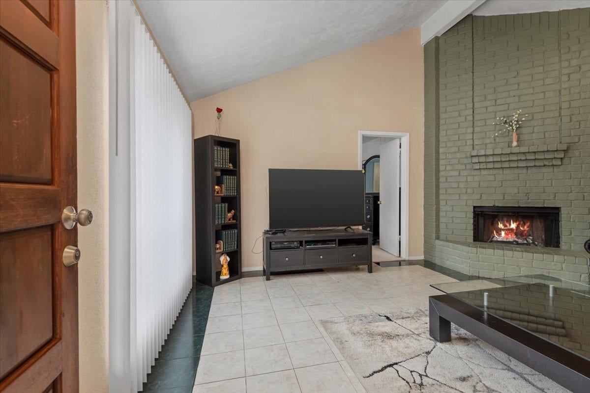 9522 Wellsworth Drive, Houston, TX 77083 Living room with vaulted ceiling, gas fireplace, tile flooring, and natural light