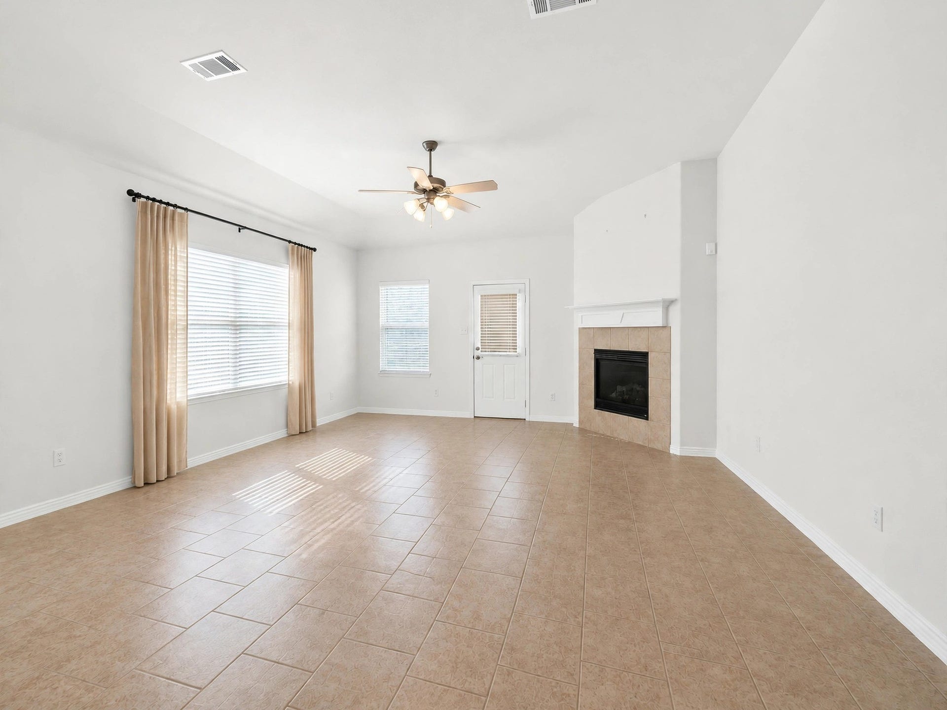 1902 Willow Ridge Ln, Fulshear, TX 77423 Spacious living area with a fireplace, ceiling fan, and large windows overlooking the backyard.