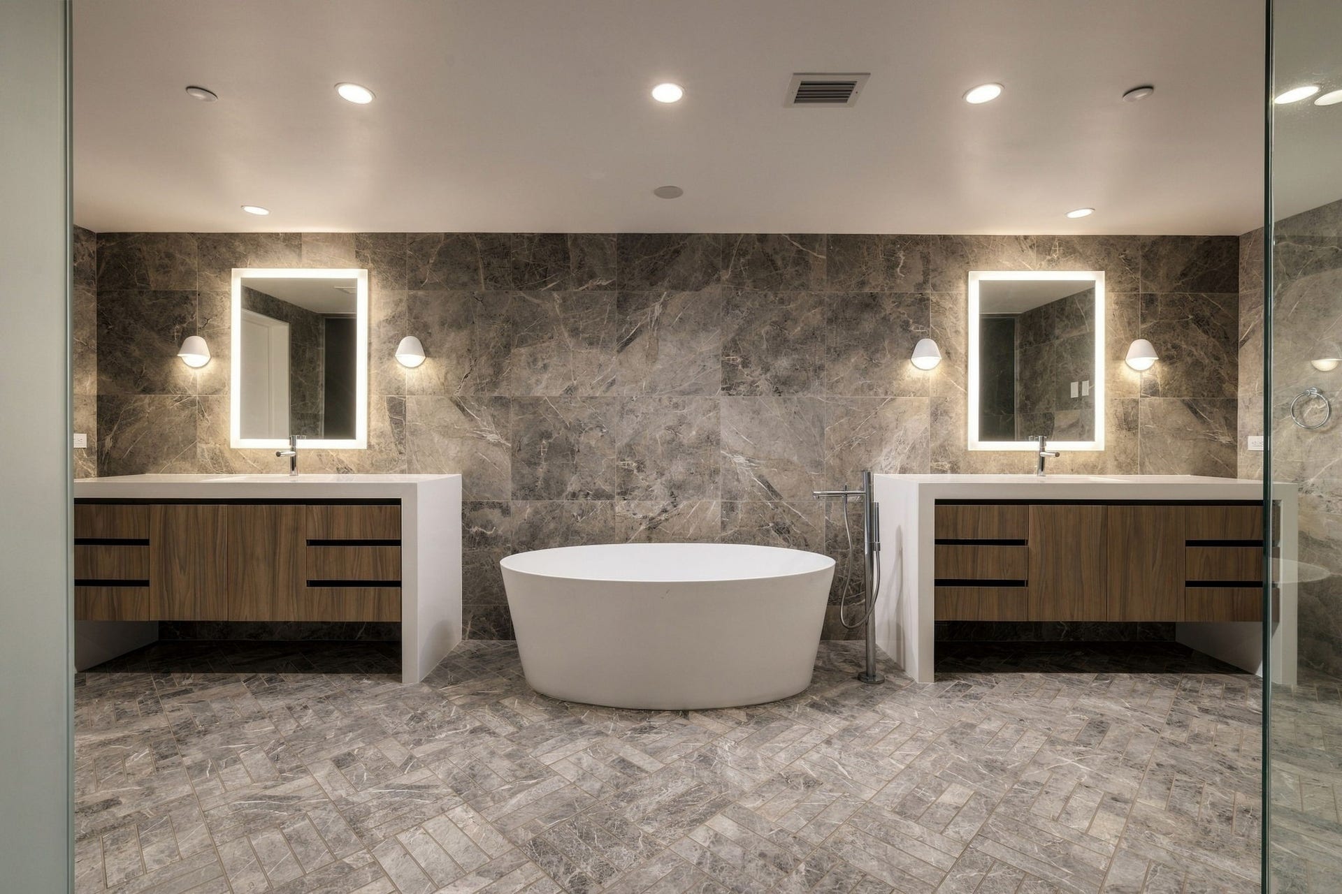 Inside the main-floor primary en suite bathroom, two wood vanities with waterfall quartz countertops and Robern medicine cabinets flank a freestanding Barclay soaking tub.