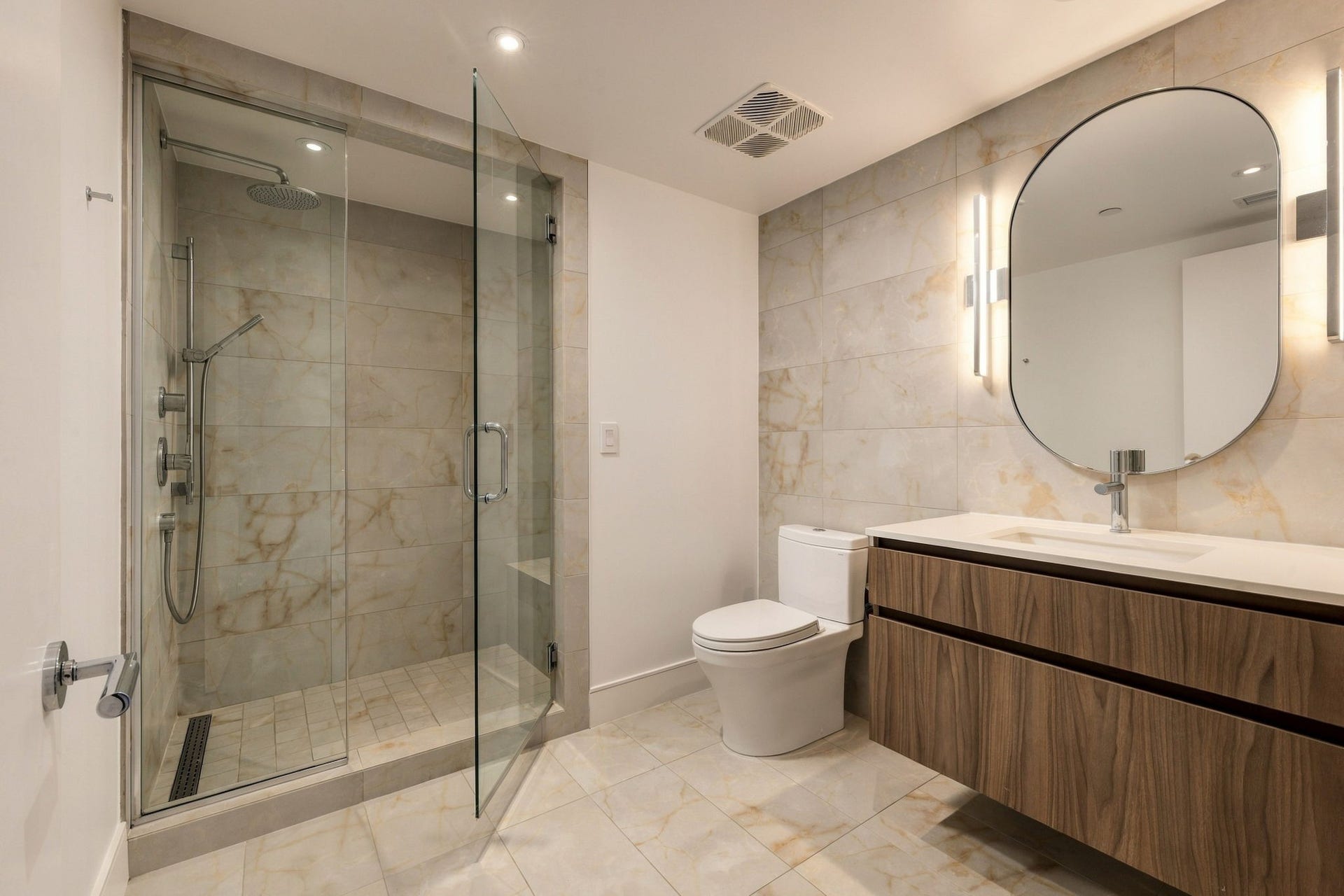 This secondary en suite bathroom is finished with floor-to-ceiling tile, a walk-in rain shower and floating vanity.