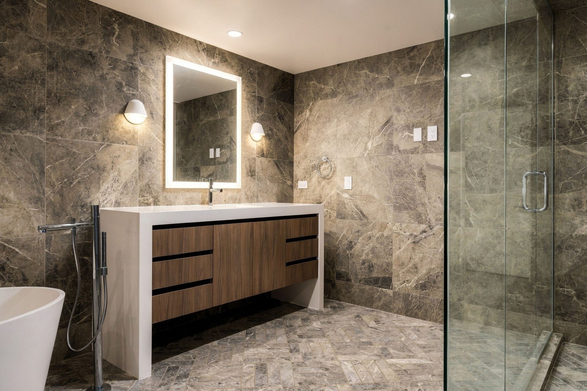 A shower, private water closet and floor-to-ceiling gray marble tile create an extraordinary spa experience in the main-floor primary en suite bathroom.