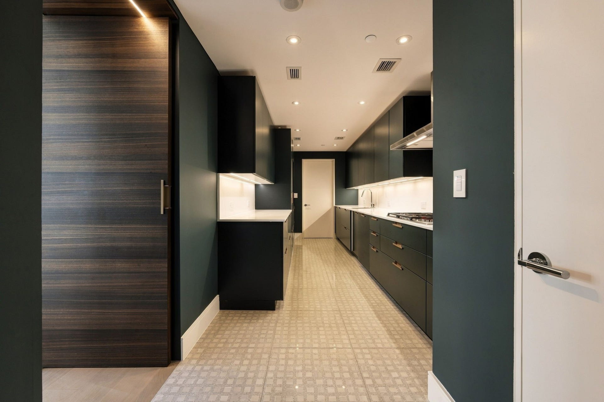 A concealed door reveals the working kitchen and storage pantry, where crisp white quartz counters show off emerald-green Cesar cabinetry. A Wolf cooktop, oven and microwave, Asko dishwasher, and Sub-Zero freezer and wine refrigerator complete the functional space. Complete with fully custom built out pantry with adjustable lighting.