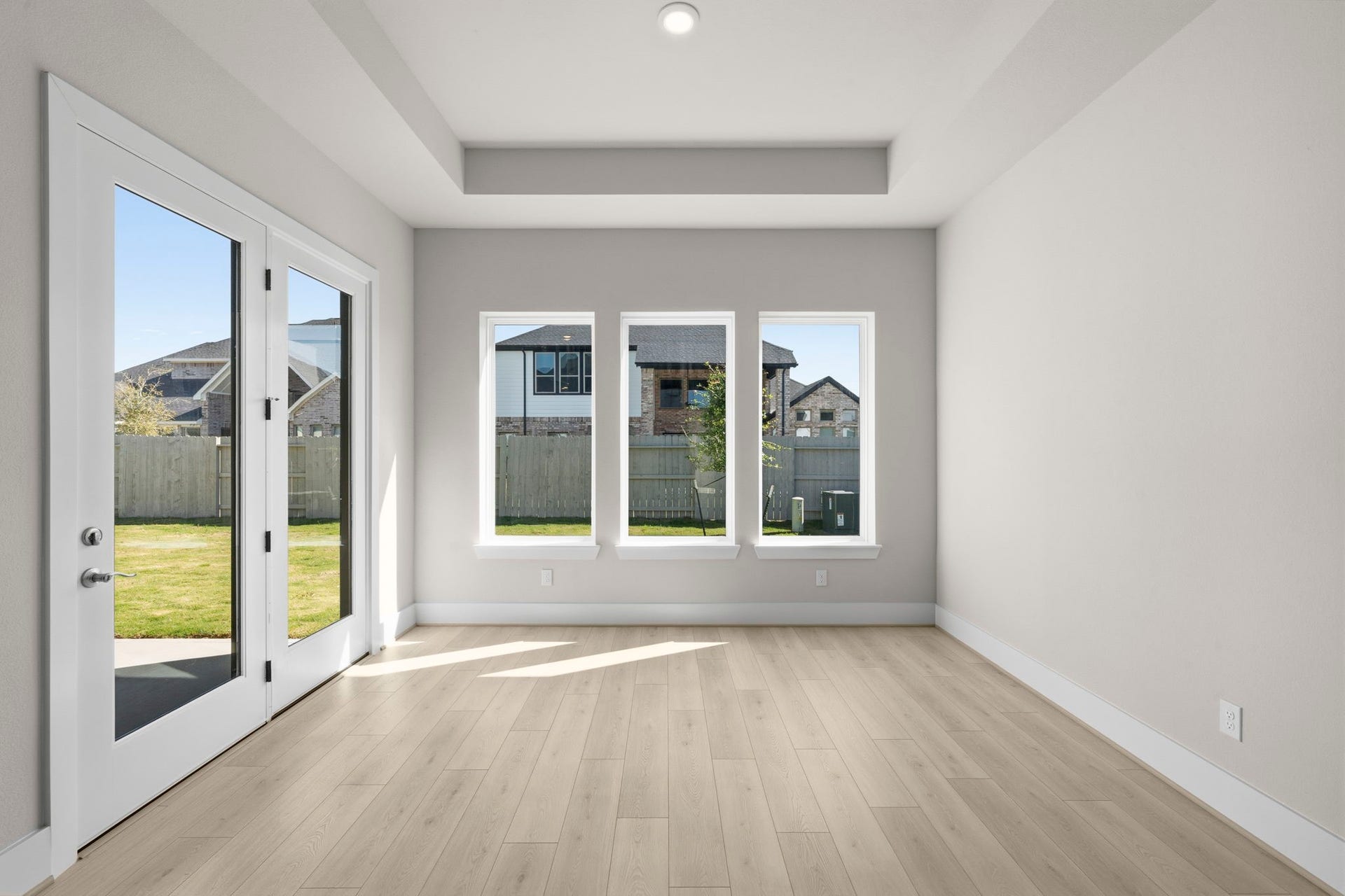 The sunroom comes with large windows and light wood flooring, offering a view of a fenced backyard. French doors provide access to the outdoor space, enhancing the open feel.