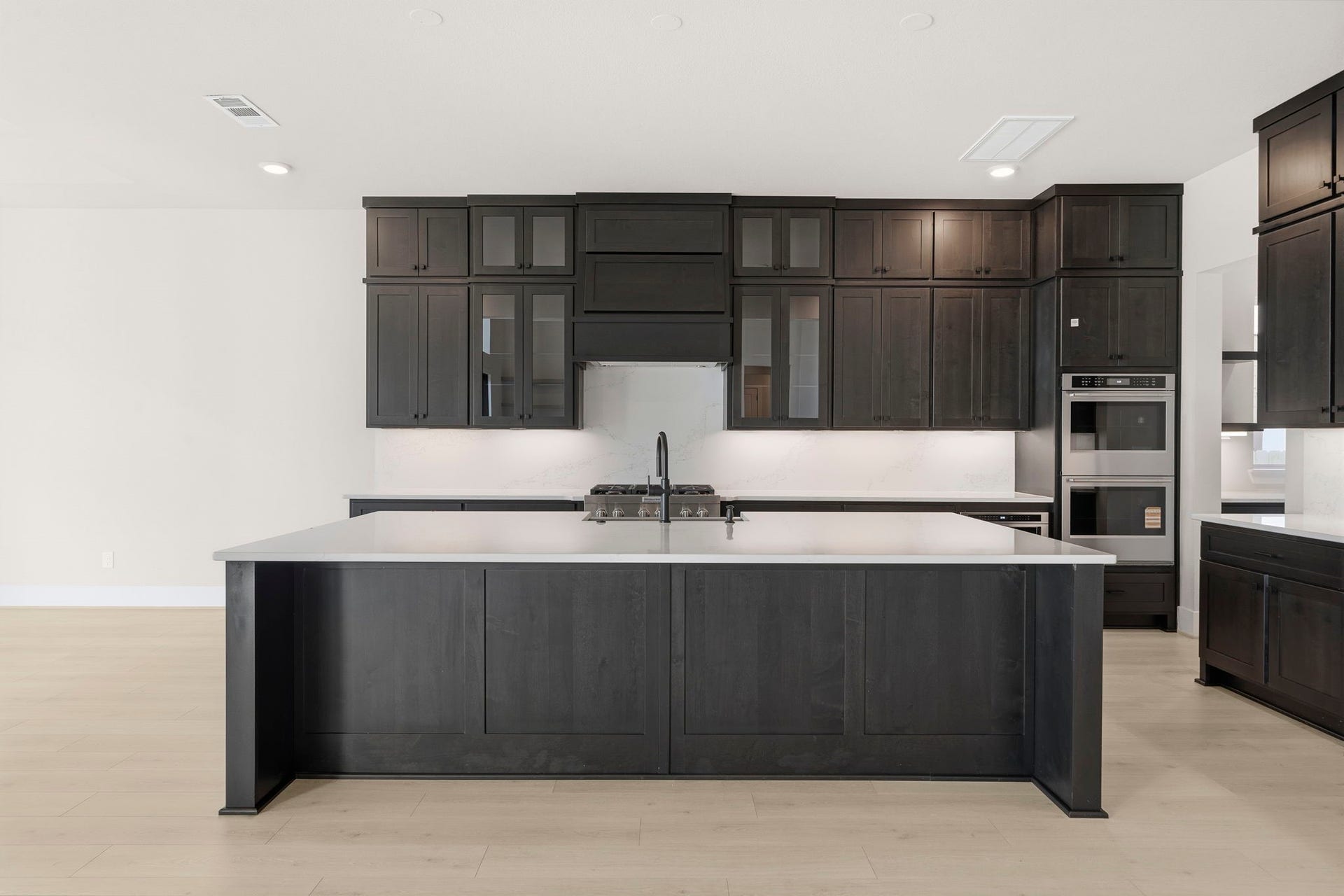 This photo showcases a modern kitchen with dark cabinetry, a large central island, and light countertops. It features built-in appliances, ample storage, and a sleek, minimalist design.