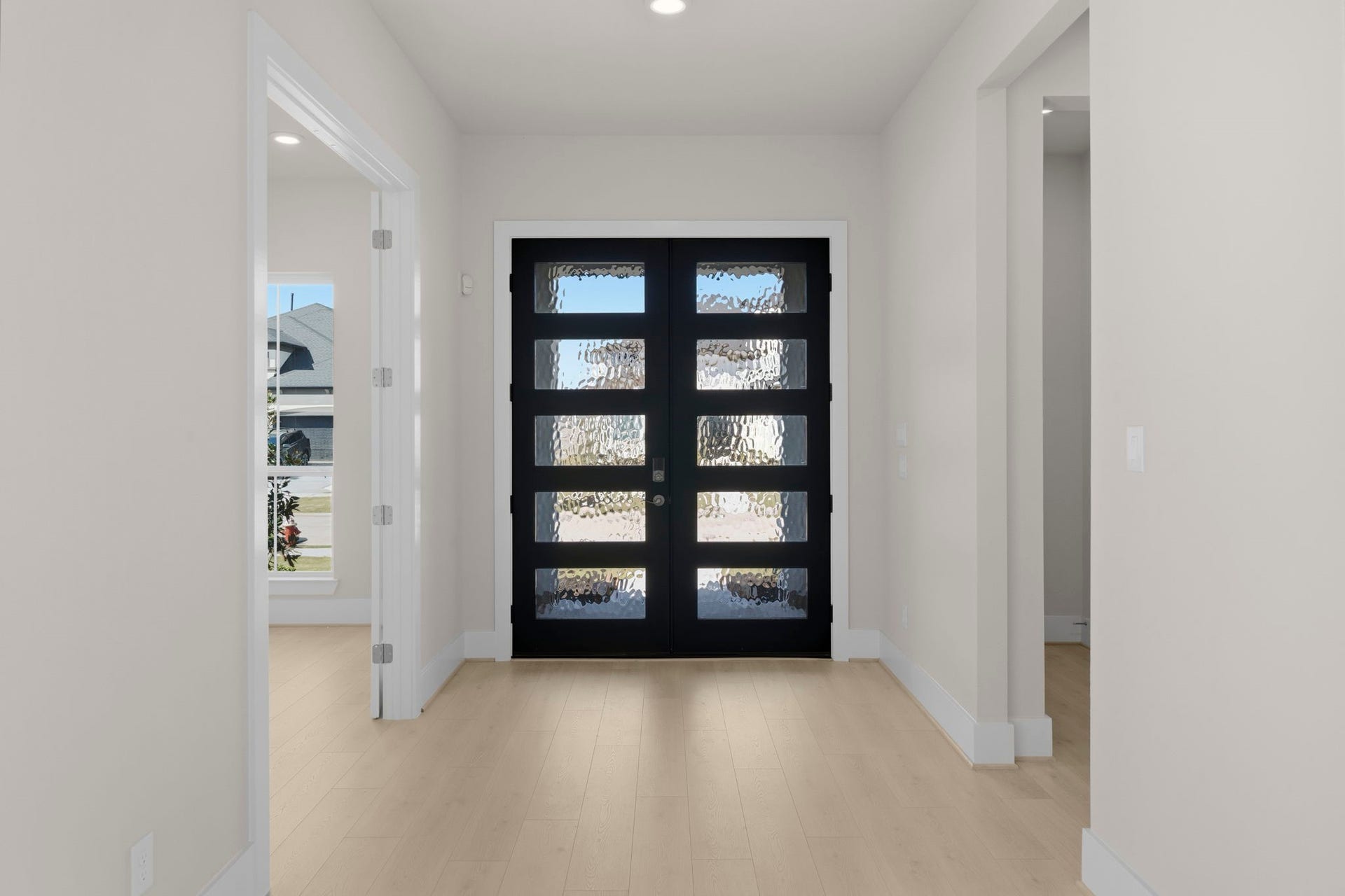 Striking black front door featuring glass panels. The hallway is bright, with light wood flooring and neutral walls, creating a welcoming and contemporary feel.
